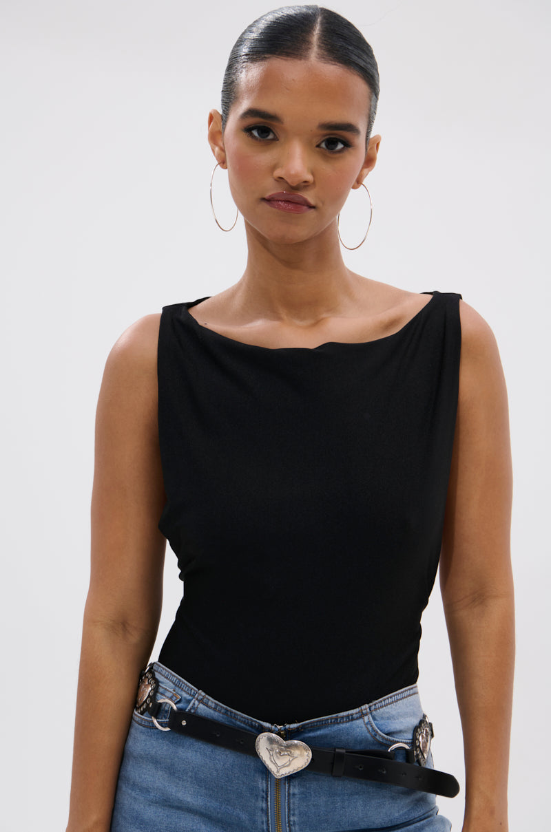 A woman with slicked-back hair, hoop earrings, blue jeans, and a black belt with a silver heart buckle models the SEXY OPEN SIDE BODYSUIT, highlighted by its curve-skimming silhouette, against a plain white background.