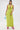 A woman poses against a white backdrop in the IN YOUR DREAMS SATIN MIDI DRESS, featuring a lime green halter style with a deep V neckline. She accessorizes with a blue beaded purse and hot pink high-heeled sandals.