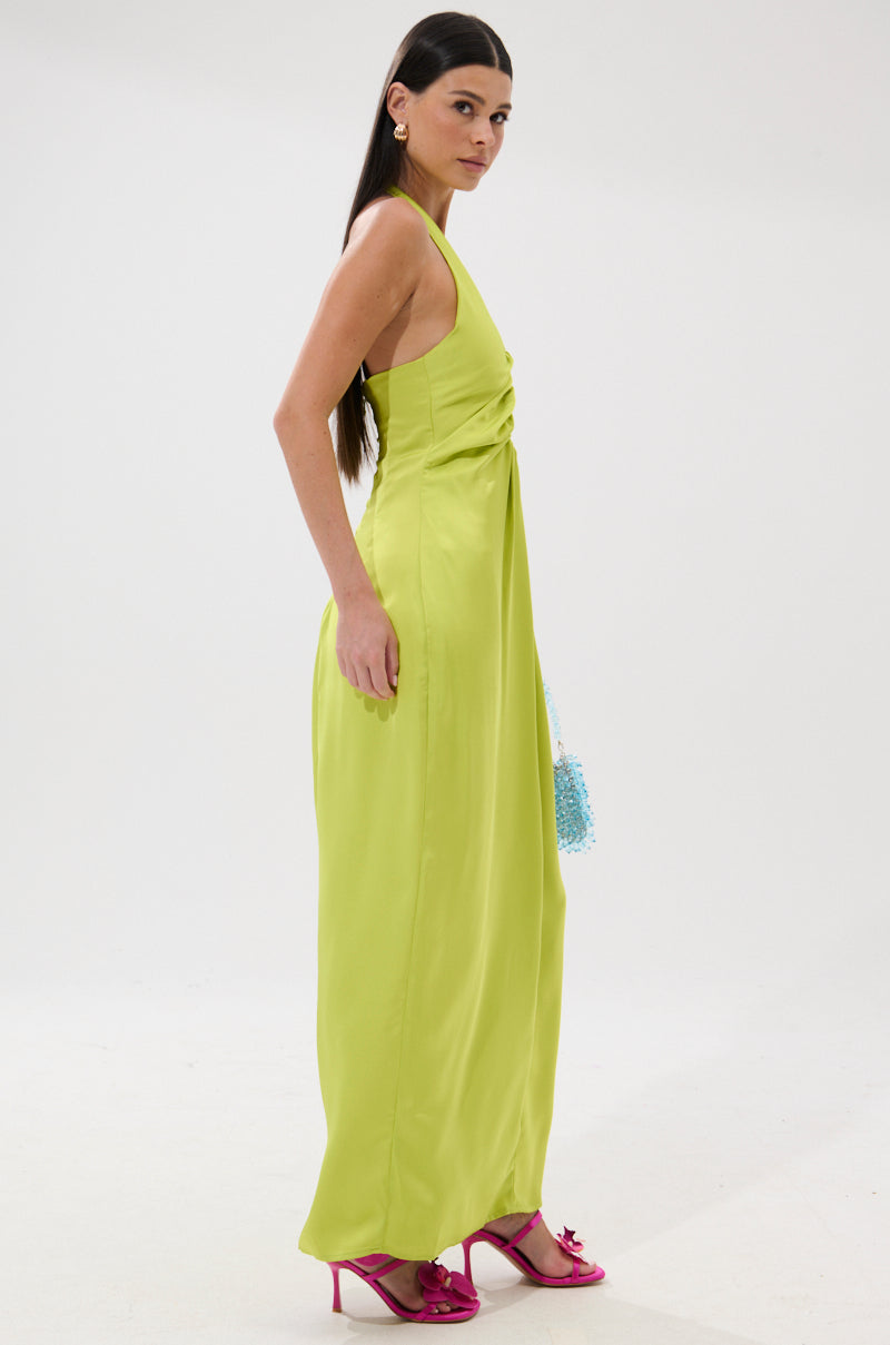 A woman with long dark hair stands sideways against a white background, wearing the IN YOUR DREAMS SATIN MIDI DRESS in lime green, hot pink heels, and holding a beaded blue clutch.