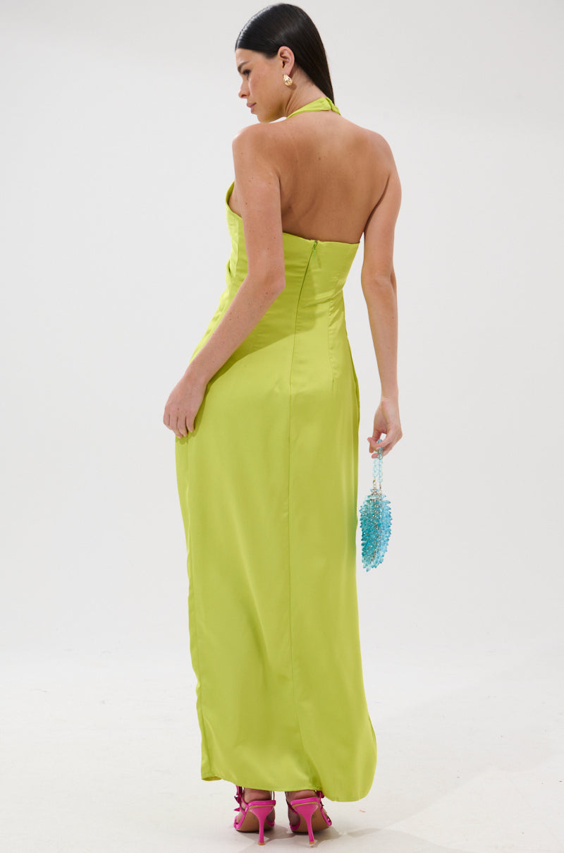 Woman facing away in the IN YOUR DREAMS SATIN MIDI DRESS in bright lime green, holding a small blue beaded handbag and wearing pink high-heeled sandals. Background is plain white.