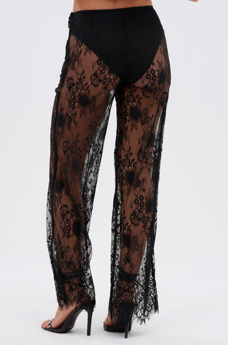 A person models the DRESSED TO IMPRESS LACE FLARE LEGGING—sheer floral lace pants over black high-waisted underwear and black heels—seen from the back against a plain white background.