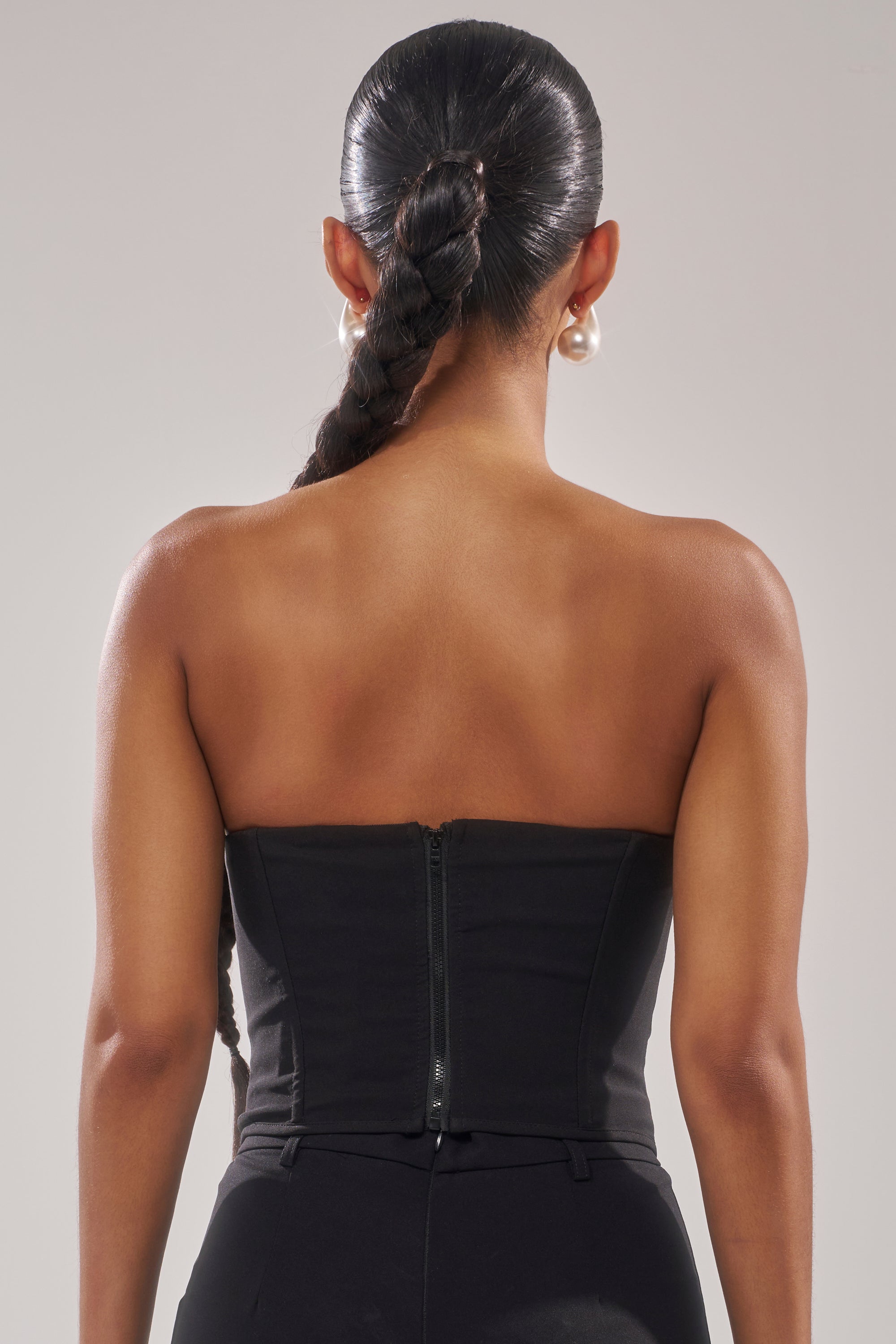 A woman with a long braided ponytail is shown from the back, wearing the NEVER YOURS ALL OVER PEARL CORSET and large pearl earrings against a neutral background. 4