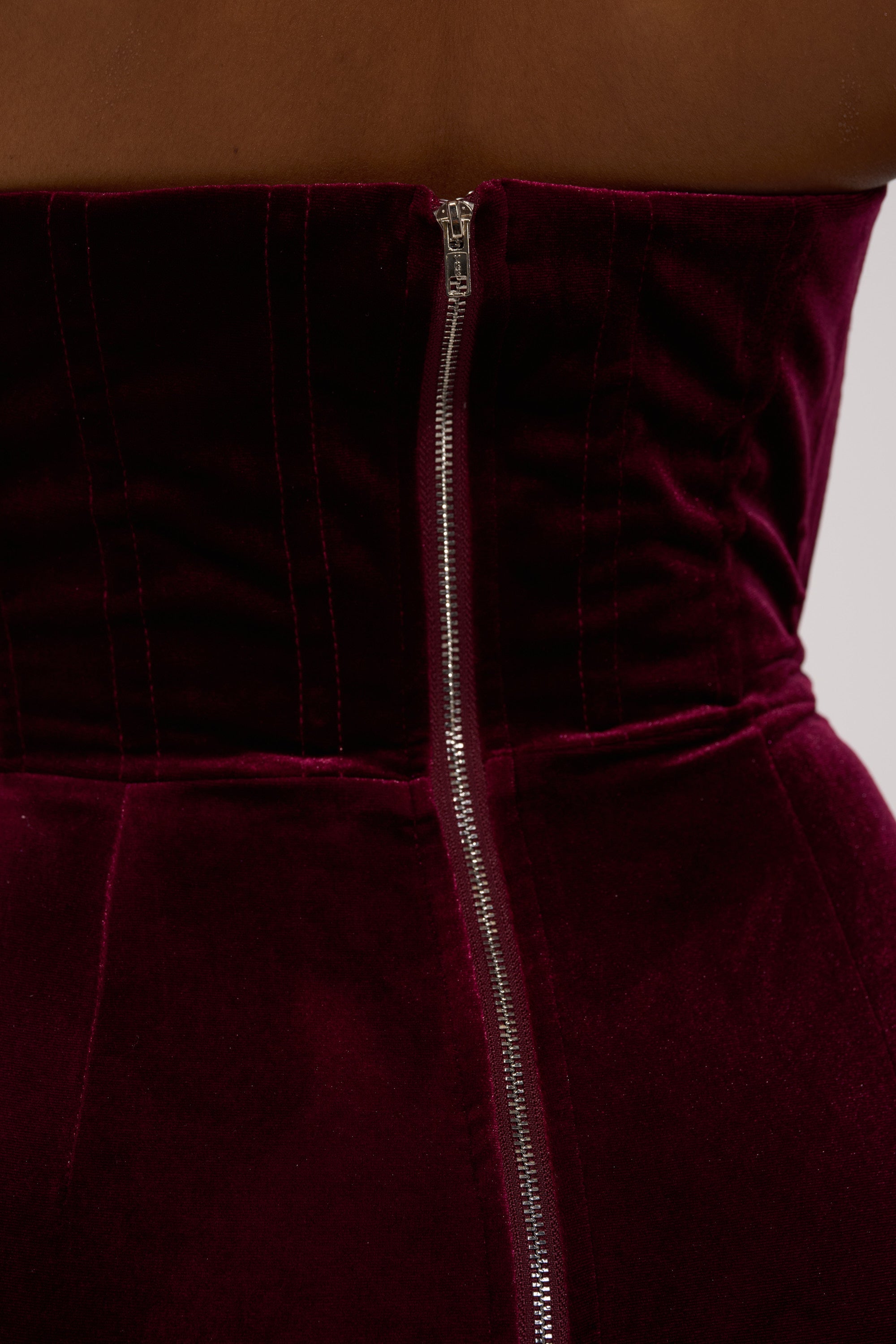 Close-up of the FEELIN THE LOVE VELVET RHINESTONE MINI DRESS back, a strapless deep burgundy velvet bodycon with vertical seams and a central visible silver zipper.