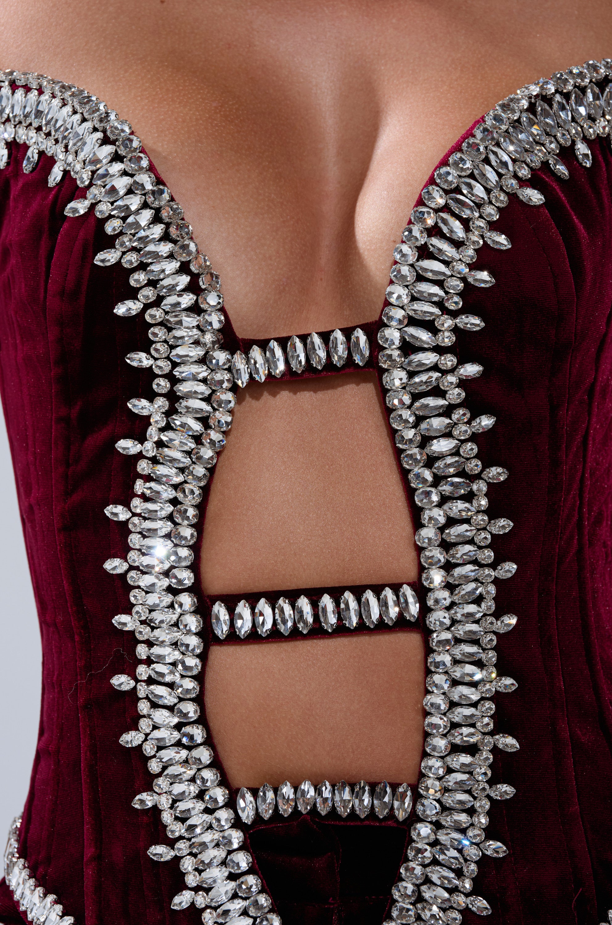 A close-up of the LUXE LIFE CORSET IN BURGUNDY, a deep red velvet piece with sparkling rhinestone rows, featuring a plunging neckline and ladder-style cut-outs that reveal skin.