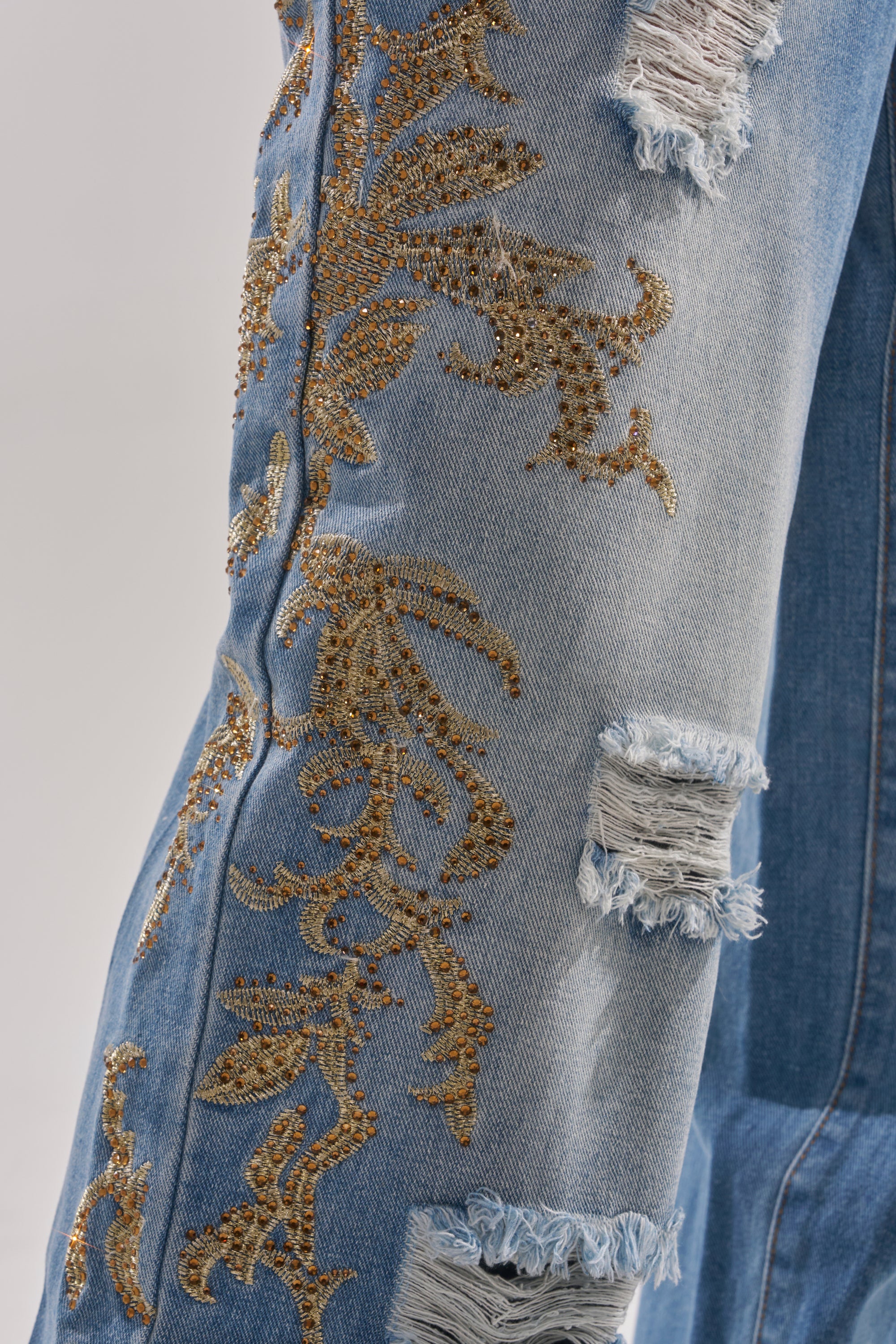 Close-up of the CLEO GOLDEN DISTRESSED STRAIGHT DENIM PANT, showcasing gold embroidered floral patterns, distressed detailing, and subtle rhinestone embellishments on blue denim. 7