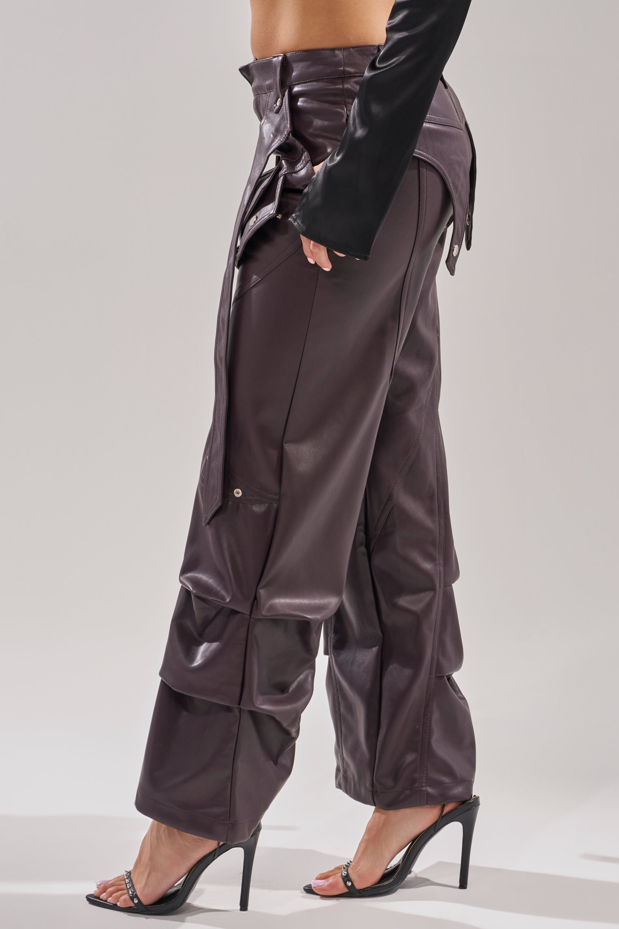 Wearing THE BEST PLUM FAUX LEATHER CARGO TROUSER—a high-rise, wide-leg cargo with flap details—styled with a black long-sleeve top and black heeled sandals, standing against a plain background. 2
