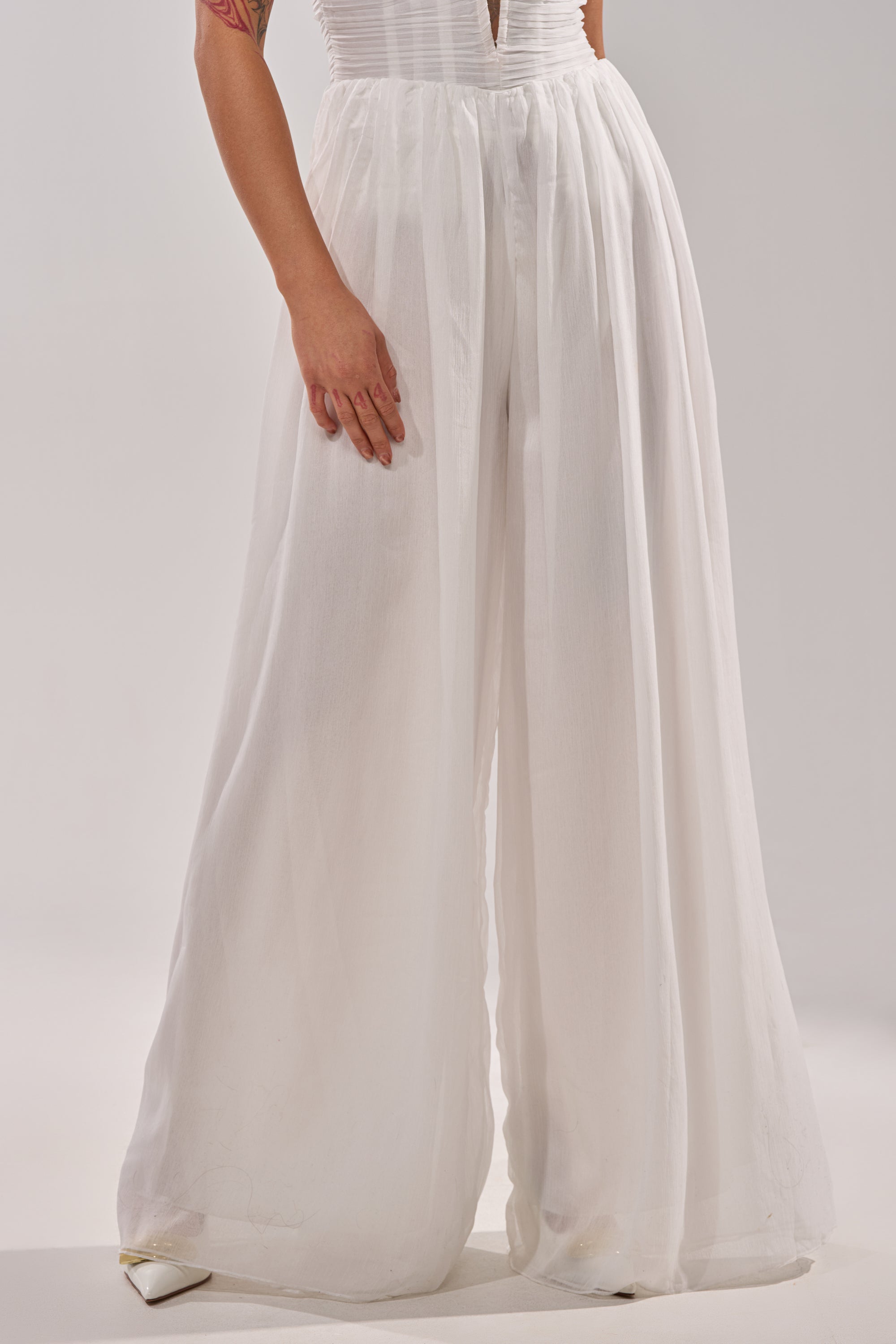 A person showcases the BEAUTIFUL WHITE PALAZZO PANT—high-waisted, sheer white—paired with white pointed-toe shoes, standing against a light plain background. Only their lower half is visible. 0