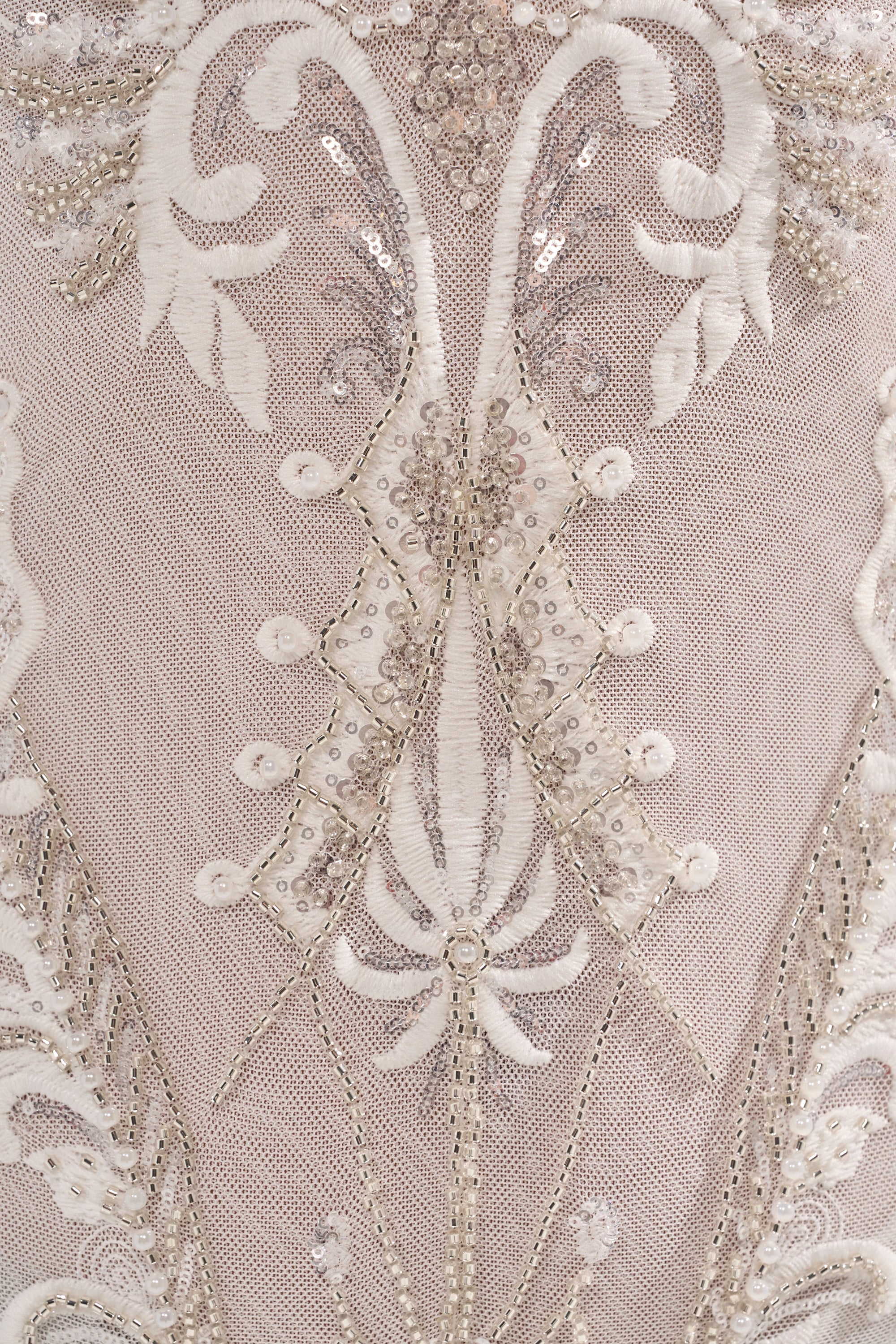 Close-up of detailed white and silver embroidery, sequins, and floral beadwork on sheer nude fabric of the WATCH ME WORK EMBELLISHED SEQUIN JUMPSUIT IN WHITE, showcasing swirling patterns and intricate design. 4