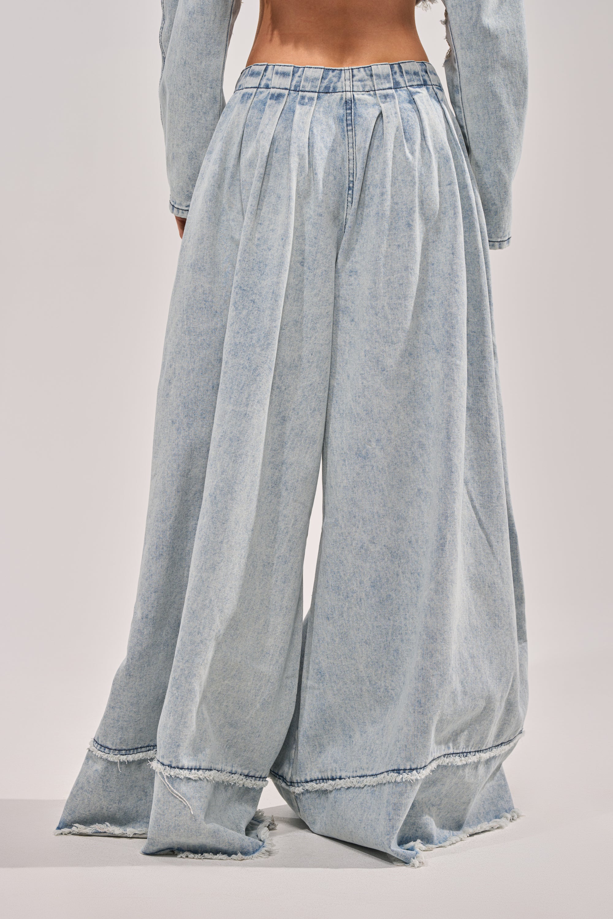 Model showcases the CAMILLE WIDE LEG DENIM—high-rise, distressed jeans with pleats and a frayed hem—photographed from the back against a plain light background. Only the statement jeans and lower torso are visible. 3