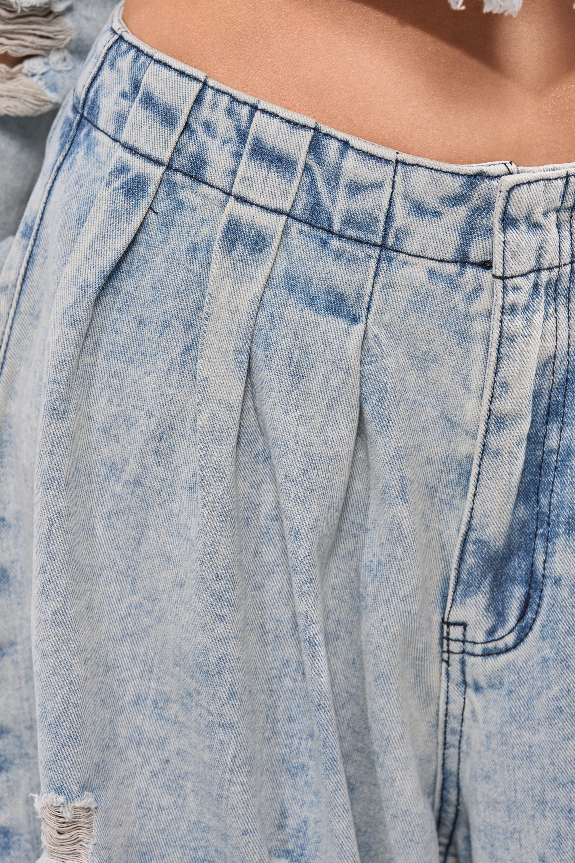 Close-up of the CAMILLE WIDE LEG DENIM in a light wash, featuring a high-rise fit, pleated details near the waistband, a metal button, and a glimpse of distressed wide-leg style at the top. 7