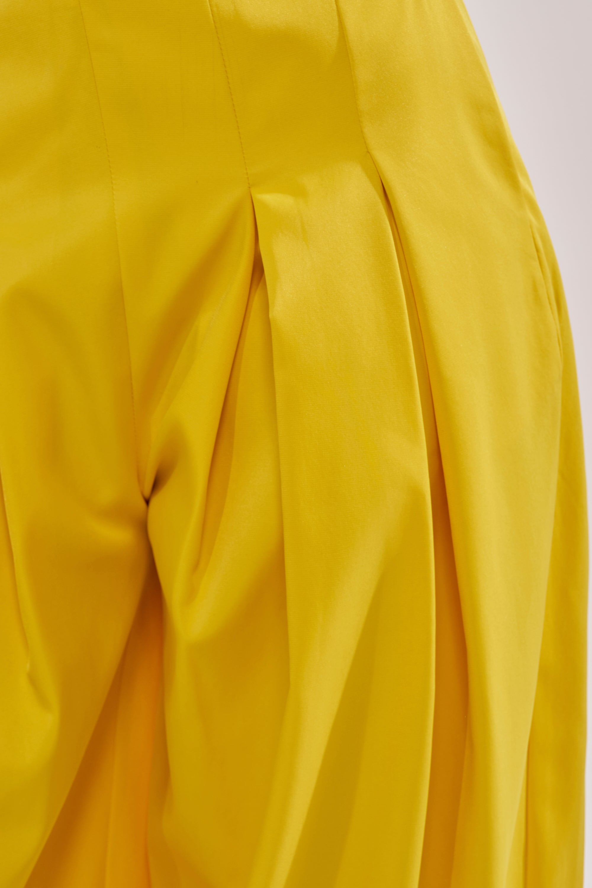 Close-up of the BRING IT ON TROUSER in yellow, showcasing wide-leg design with pleated detailing, high-rise fit, soft folds, and a smooth texture. 8