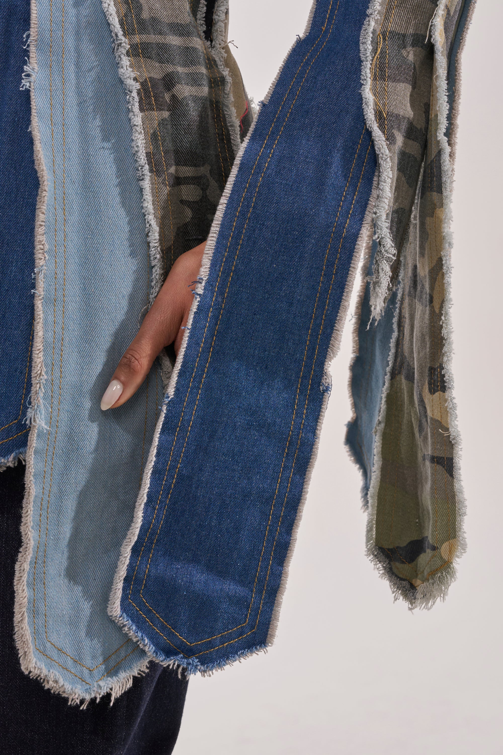 A close-up of a hand on a hip showcases the HERE FOR IT PATCHWORK BLAZER, featuring frayed patchwork fabric in denim blue and camouflage with visible stitching and raw edges. 6