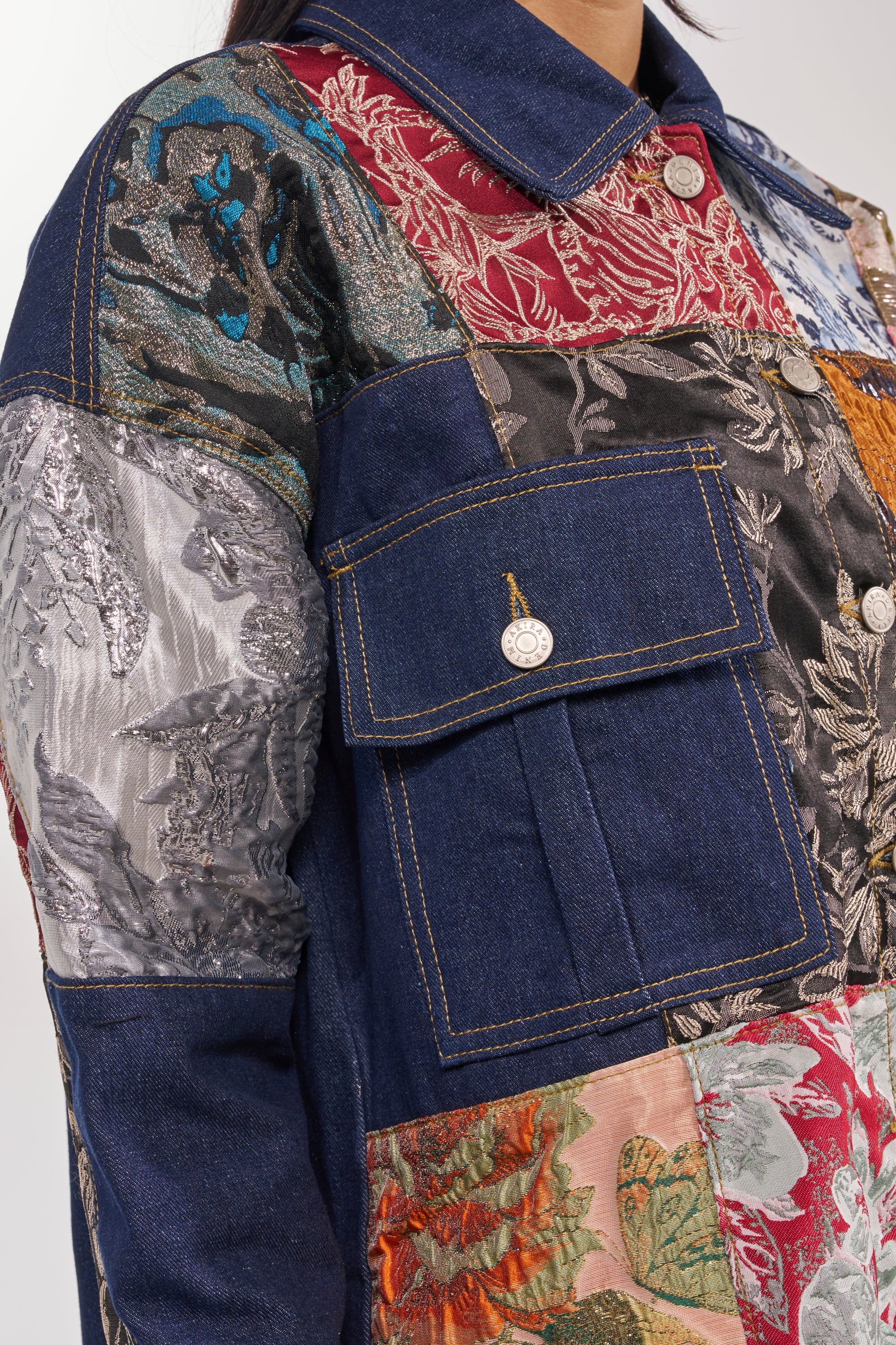 Close-up of the EMOTIONLESS BUTTON DOWN, featuring metallic brocade patchwork with colorful textures—denim, floral, and more—plus utility chest pockets and button details for a stylish finish. 10