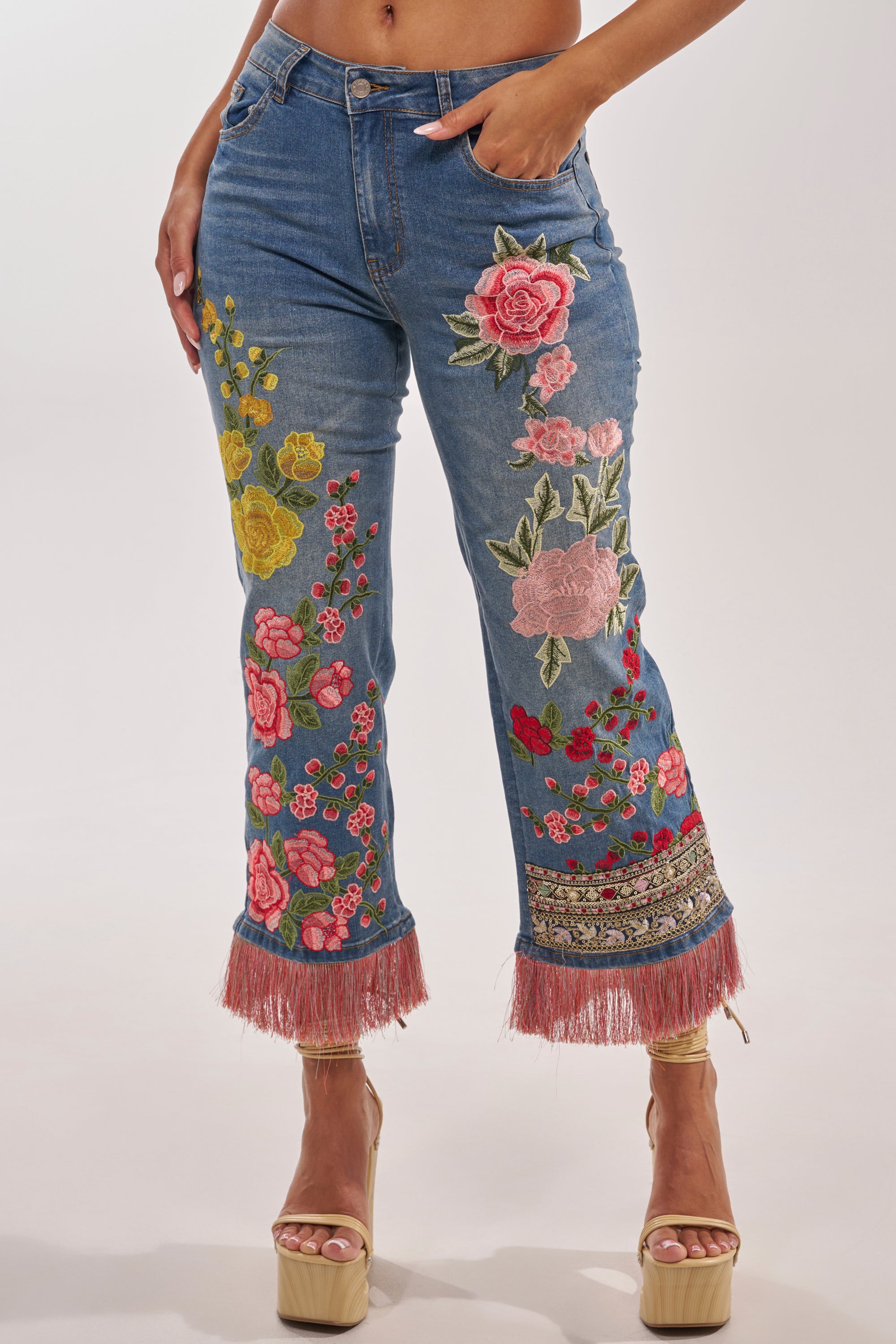 Wearing the FLORAL FOR DAYS STRAIGHT LEG DENIM with colorful floral embroidery and pink fringed hems, styled with beige high-heeled platform sandals for a chic boho-luxe vibe. 1