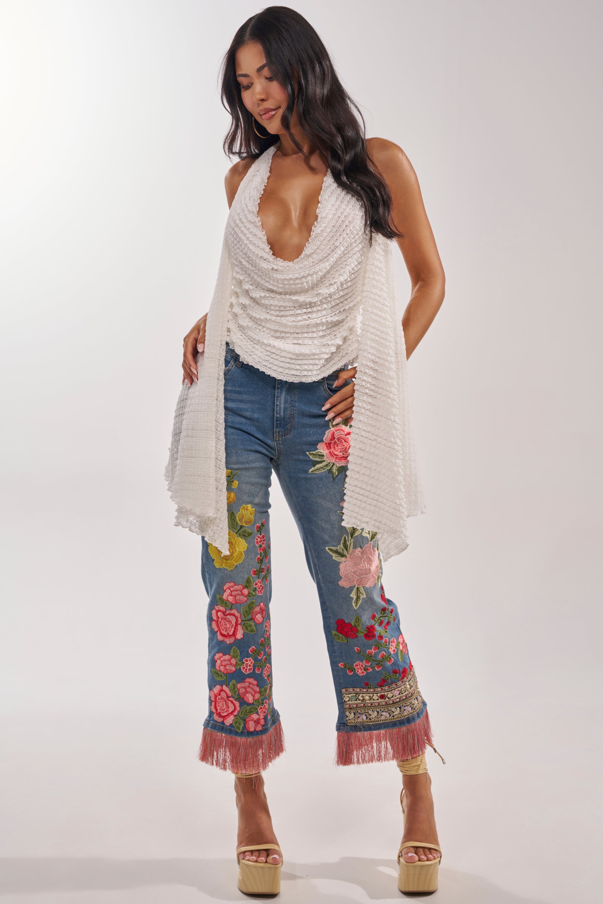 A woman stands in platform heels against a plain background, wearing a sleeveless white cowl-neck top and FLORAL FOR DAYS STRAIGHT LEG DENIM, featuring colorful floral embroidery and pink fringe at the cuffs. 6