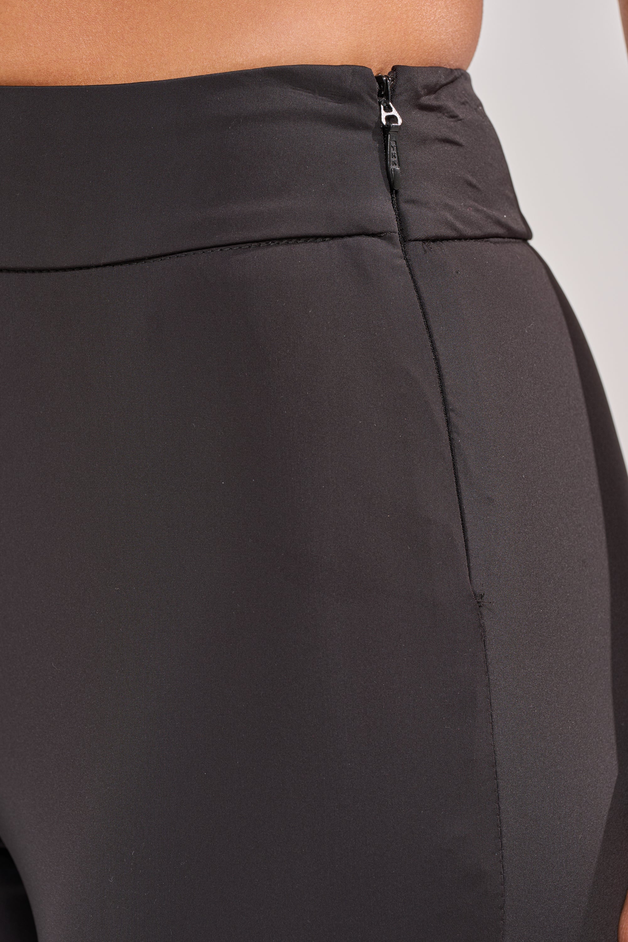 Close-up of a person wearing the CHECK IT OUT GROMMET FLARE LEGGING, featuring black flare design, high-rise waistband, and a side zipper detail. The fabric is smooth and slightly reflective. 6