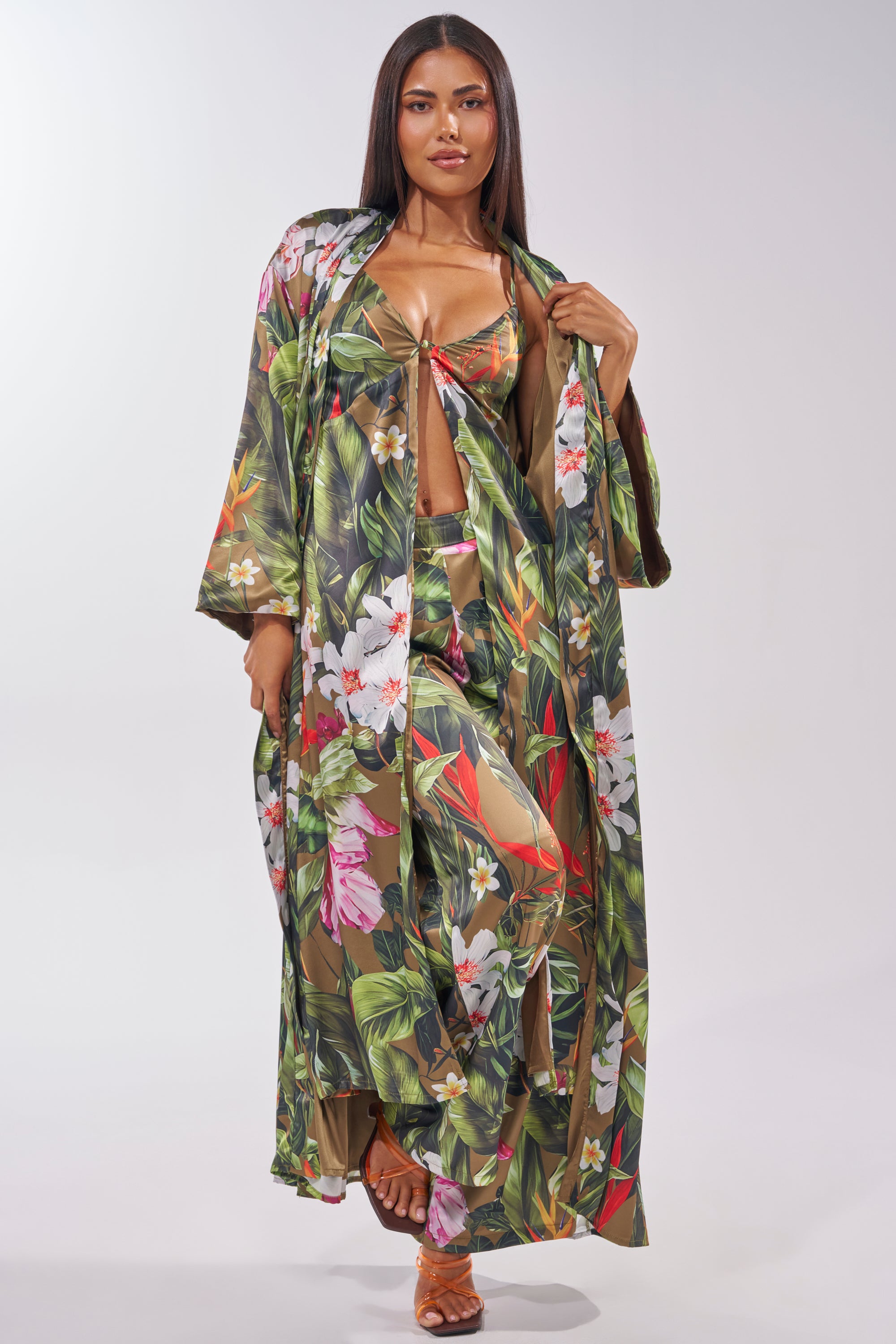 A woman stands confidently against a plain background in a long robe and crop top, paired with the INTO THE WILD FLORAL TROUSER—satin trousers featuring a tropical print, perfect for stylish summer looks. 9