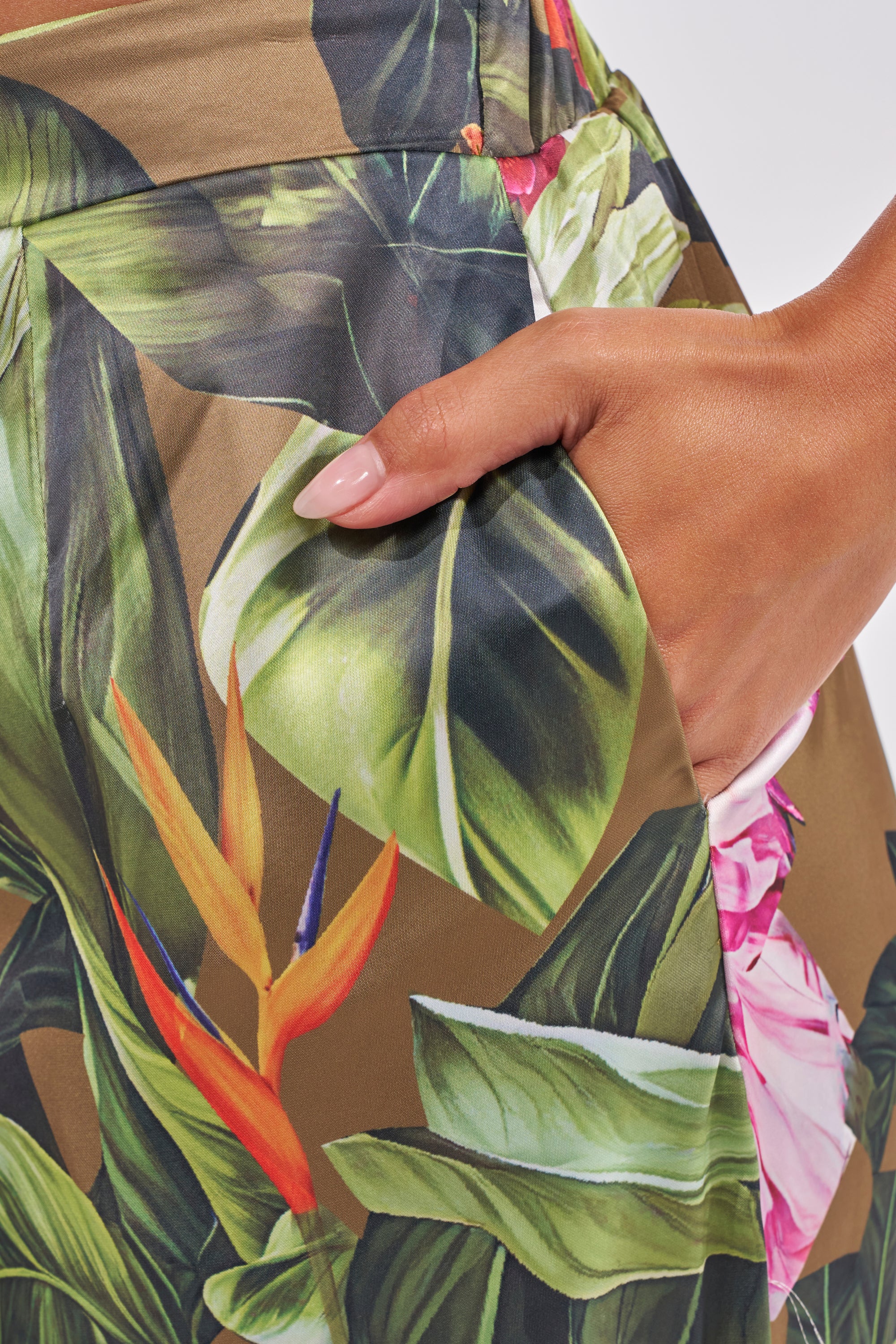 A close-up of manicured nails resting in the pocket of the INTO THE WILD FLORAL TROUSER, featuring a breezy wide-leg fit and vibrant tropical floral and leaf print. 10