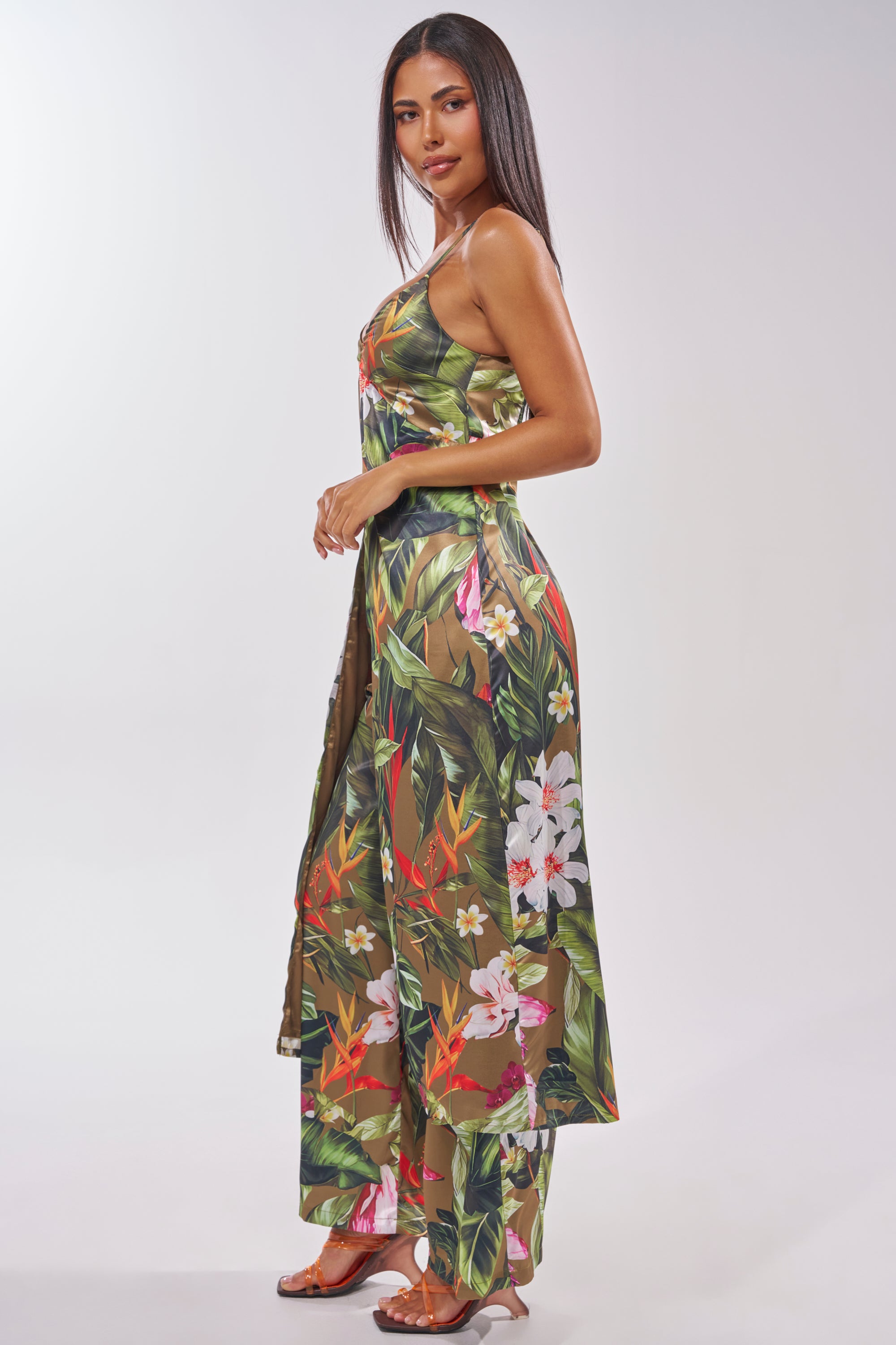 A woman in profile wears the INTO THE WILD FLORAL BLOUSE with long straight hair and heeled sandals, posing against a plain light background—the blouse's vibrant floral print is ideal for stylish summer looks. 3
