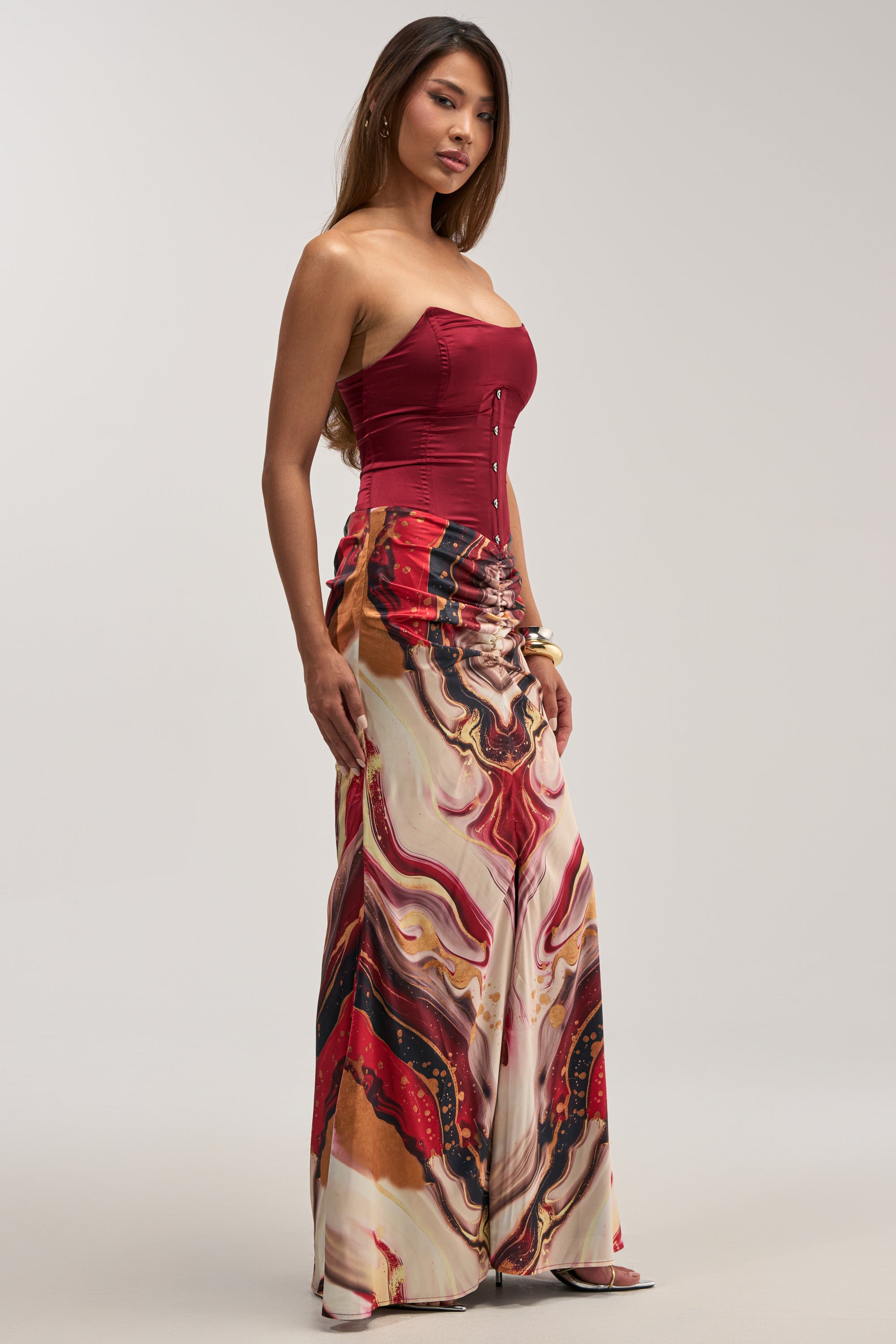 A woman wearing the SAMARA ABSTRACT MAXI DRESS IN RED MULTI stands against a plain background, looking slightly to the side.