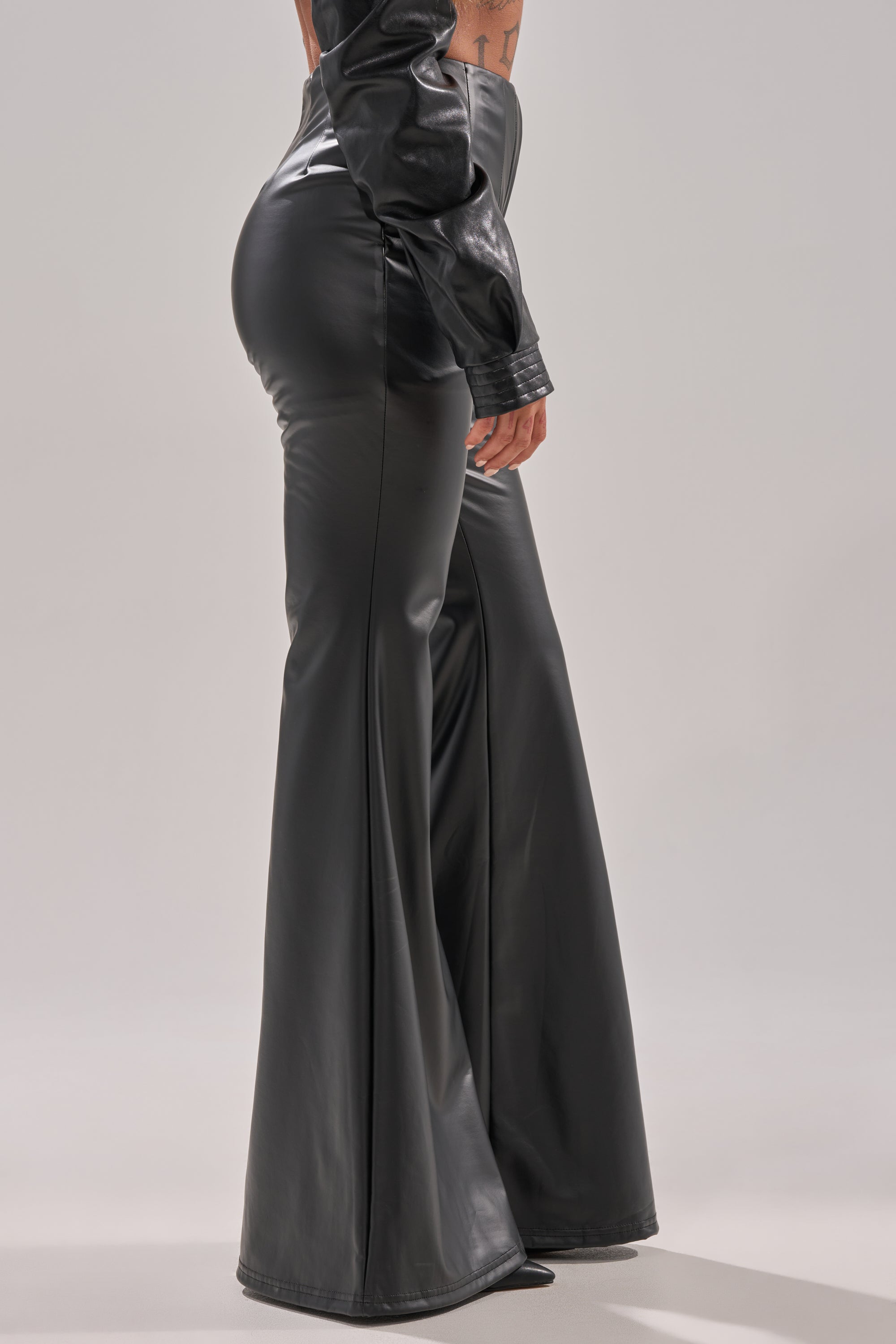A person models the DONT CRY BABY GIRL FAUX LEATHER FLARE TROUSER with a matching jacket, showing side and back views against a plain light gray background.