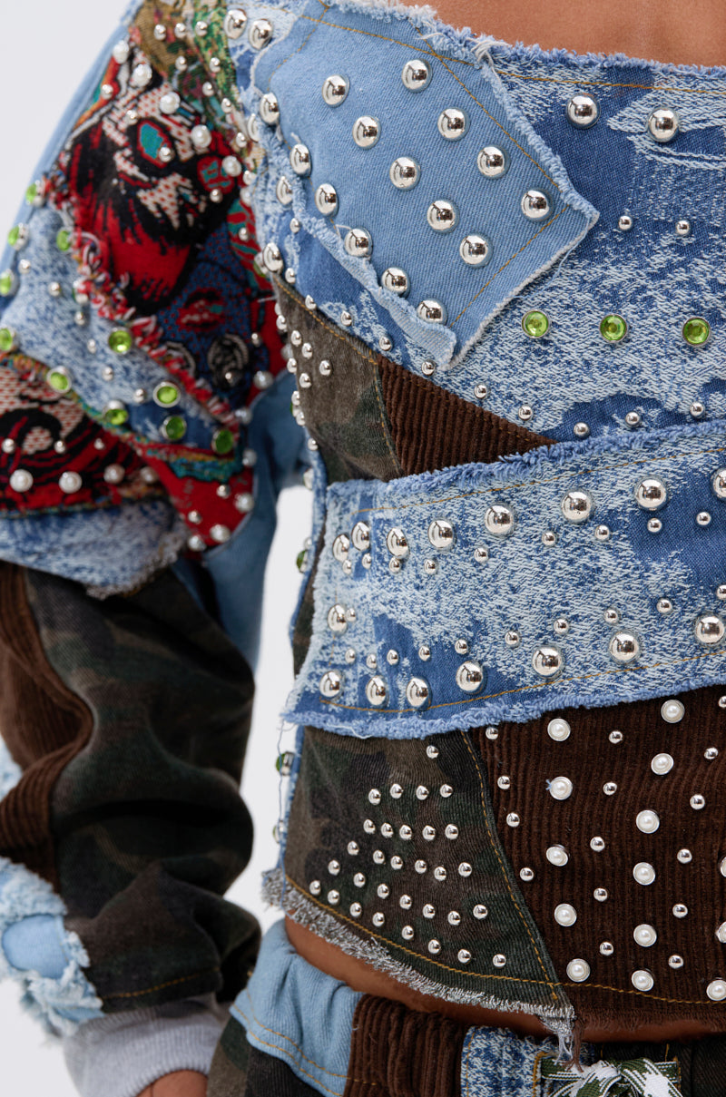 Close-up of a person wearing the CALL ME CRAZY PATCHWORK OFF THE SHOULDER SWEATSHIRT, featuring eclectic streetwear style with vibrant colors, mixed materials, textured stitching, and unique decorative details.