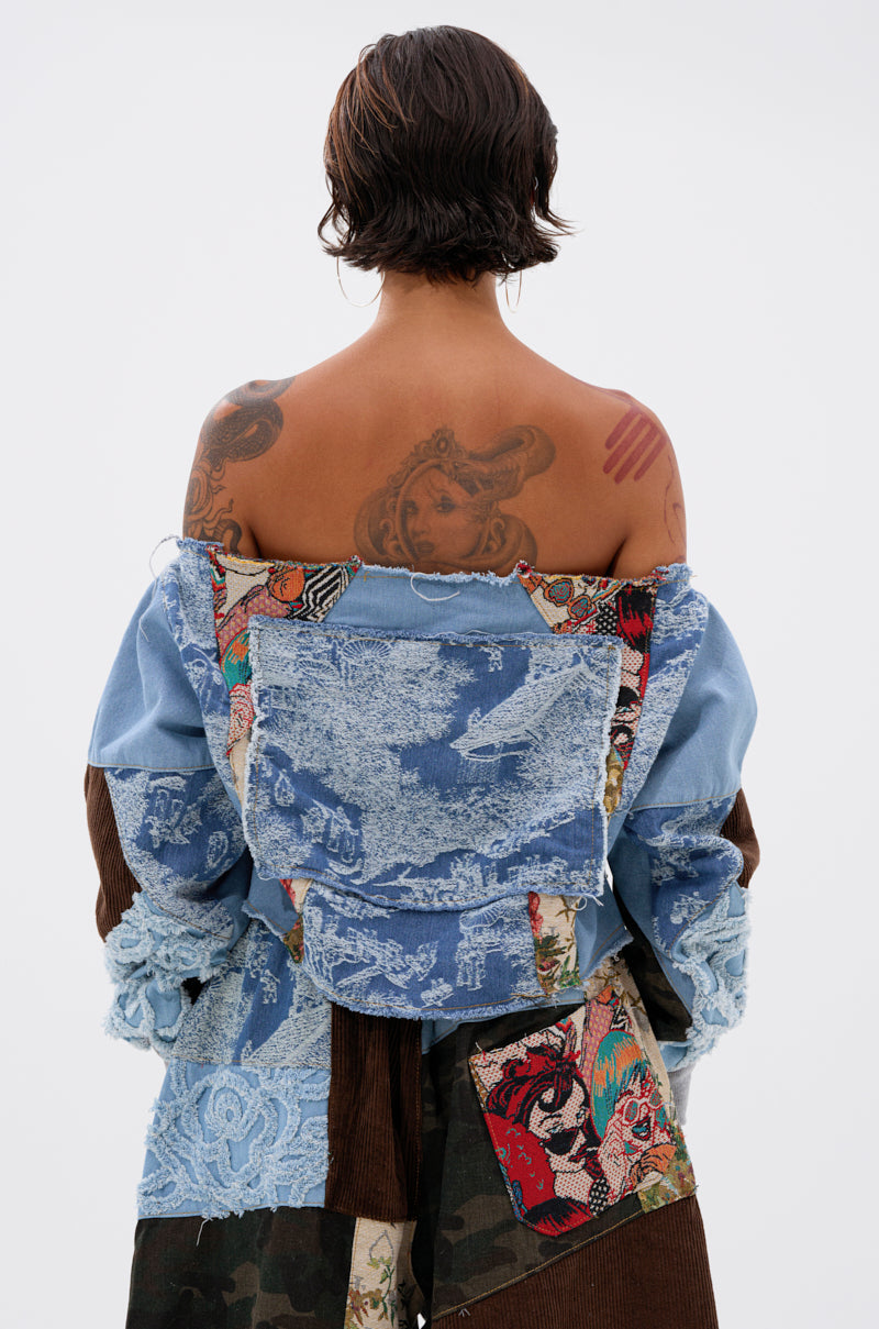 Seen from behind, a person with short dark wet hair models the CALL ME CRAZY PATCHWORK OFF THE SHOULDER SWEATSHIRT, which features blue lace, corduroy, camouflage, and tapestry patterns. Colorful tattoos cover their upper back and arms.