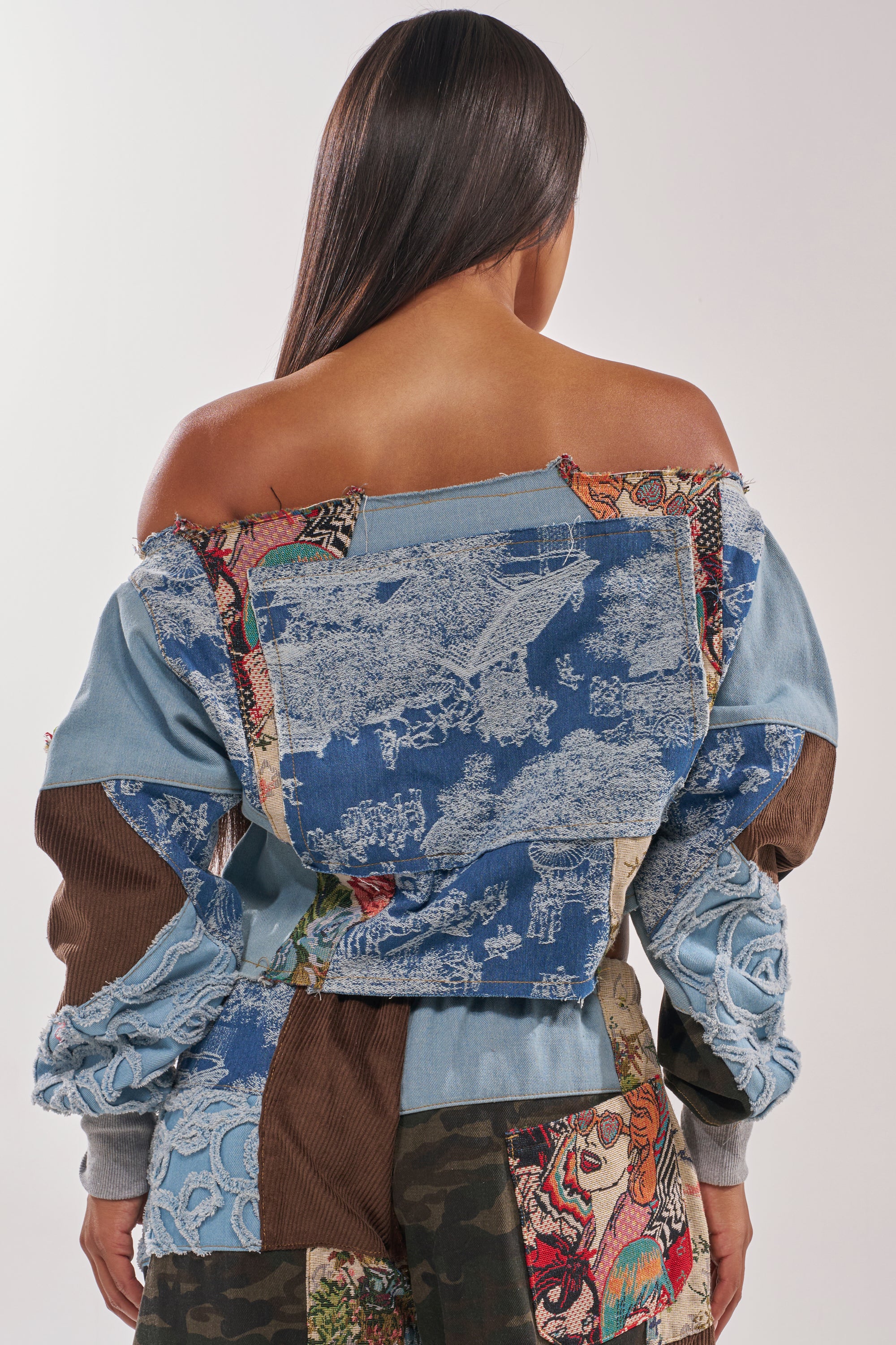 A person with long straight hair, seen from behind, wears the CALL ME CRAZY PATCHWORK OFF THE SHOULDER SWEATSHIRT and matching pants in denim, corduroy, tapestry, and camo patterns—a bold mix of streetwear colors and textures. 5