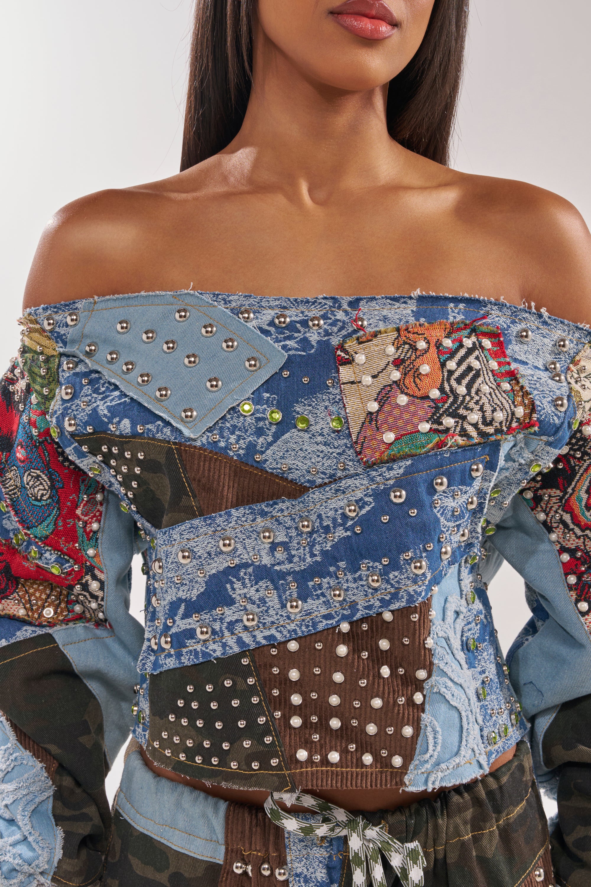 A woman wears the CALL ME CRAZY PATCHWORK OFF THE SHOULDER SWEATSHIRT, featuring studs, lace, and colorful fabric patches. The image is cropped from her shoulders to her waist. 8