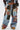 A person wears the CALL EM CRAZY PATCHWORK JOGGER—streetwear-inspired, high-rise joggers featuring a drawstring waist and wide-leg silhouette with denim, camo, floral, lace, and studded patches—paired with tan platform shoes.