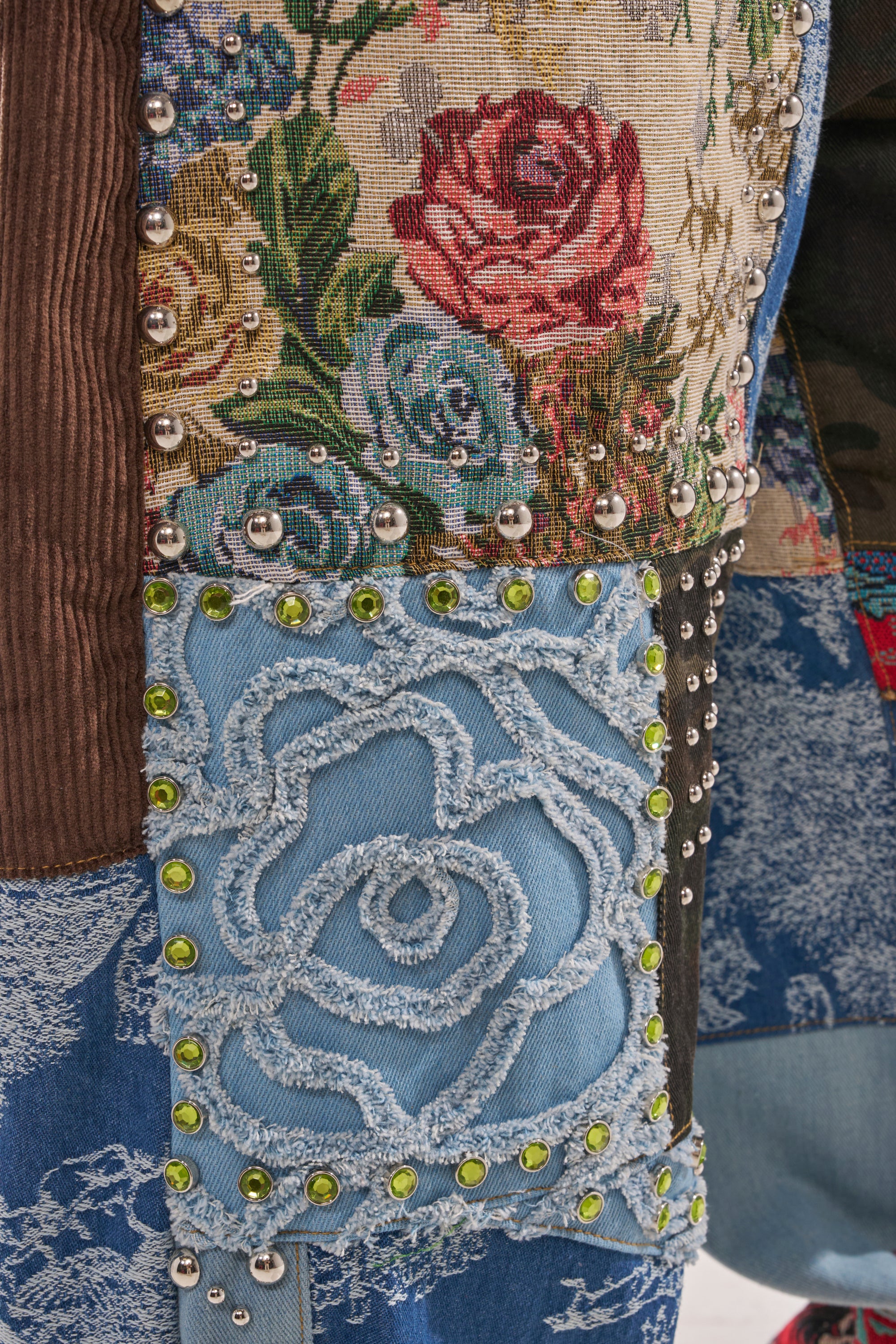 A close-up of the CALL EM CRAZY PATCHWORK JOGGER fabric highlights floral patterns, denim with an embroidered rose, shiny metal studs, and green rhinestones for a vibrant mix of textures and eye-catching details. 8
