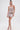 A woman showcases the SPARKLE QUEEN SEQUIN MINI SKIRT—a shiny, light pink sequin mini skirt with side cutout—styled with gold strappy heels and gold arm jewelry, standing against a plain white background for a high-glam look.