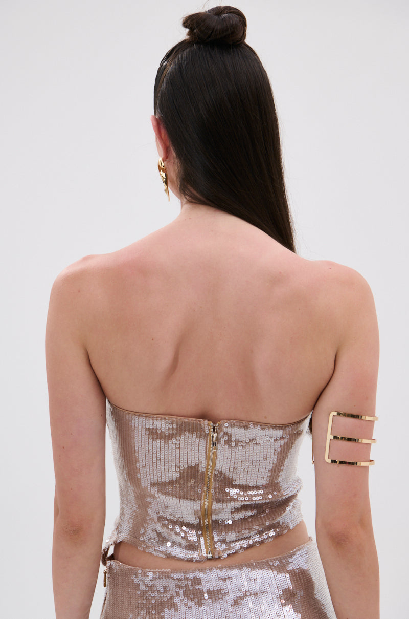 A woman with long dark hair in a topknot is shown from the back, wearing the SPARKLE QUEEN SEQUIN BLOUSE with a strapless neckline and metallic back zipper, her fair skin contrasting against a plain white background.