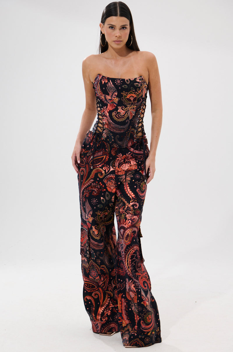 A woman models the FALL VIBES BROCADE TROUSER, featuring an ultra-wide leg and bold metallic autumnal print, set against a plain white background.