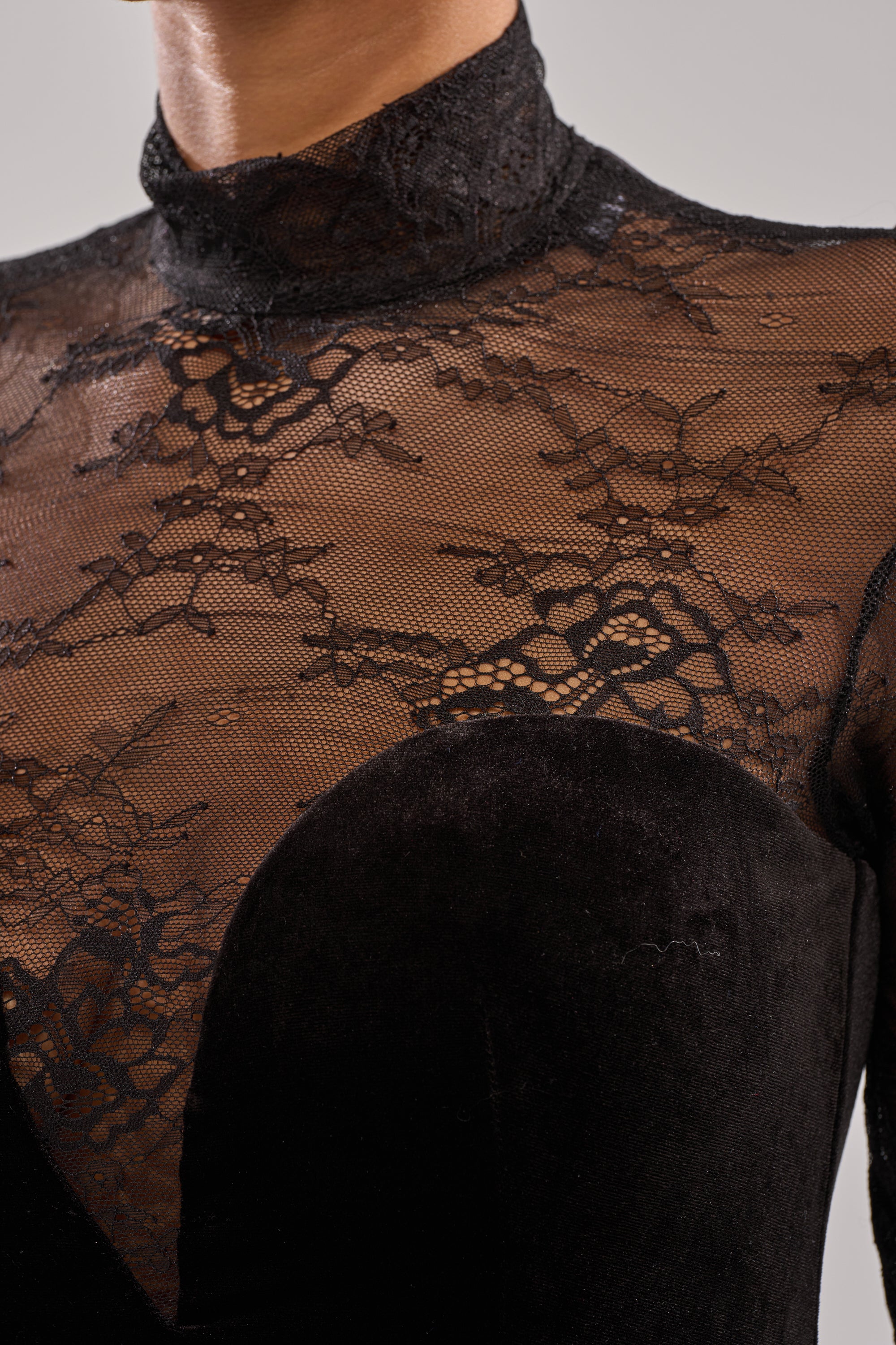 A close-up of a person wearing the DRESSED TO IMPRESS LACE MINI DRESS, a black velvet LBD with a sheer lace high neckline and floral lace bodice that adds an elegant pattern over the shoulders and collarbone.