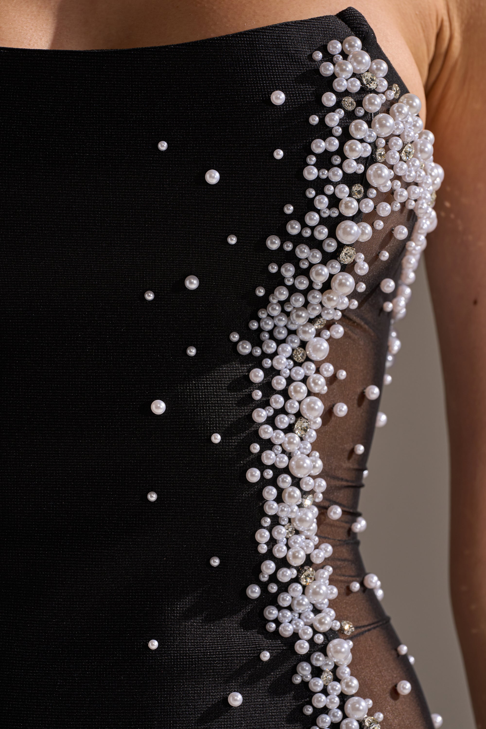 Close-up of the CHAMPAGNE EDIT RHINESTONE MIDI DRESS, a strapless black bandage dress with clusters of white pearls and rhinestones on a sheer mesh side panel, showcasing its intricate and elegant beadwork.