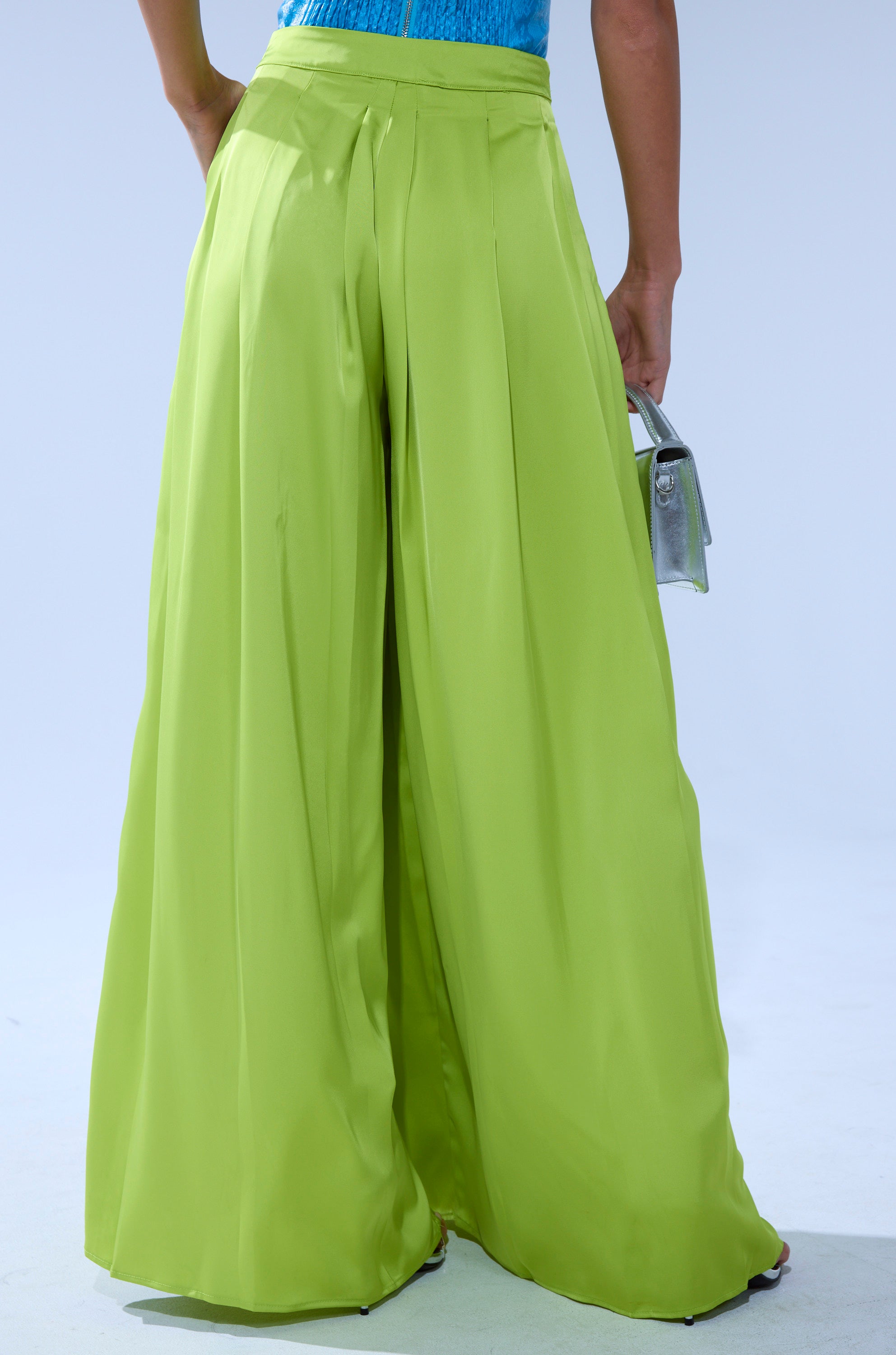 A person is shown from the back against a light background, wearing the CHARTREUSE PLEATED PALAZZO PANT and holding a small silver handbag. 4