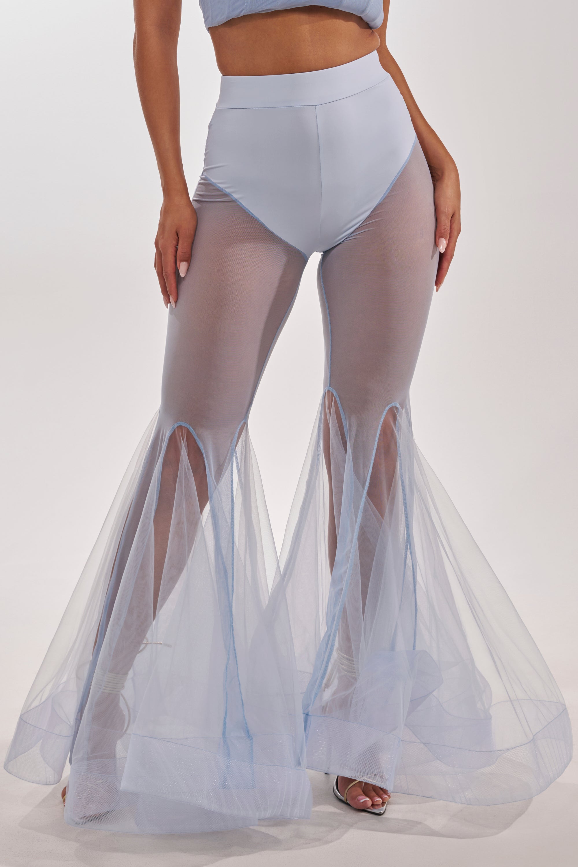 Wearing the FEELING BLUE MESH FLARE PANT—high-waisted blue sheer mesh flares with solid briefs underneath and open-toe heels—this look features a subtle mermaid-inspired silhouette against a plain white backdrop. 2