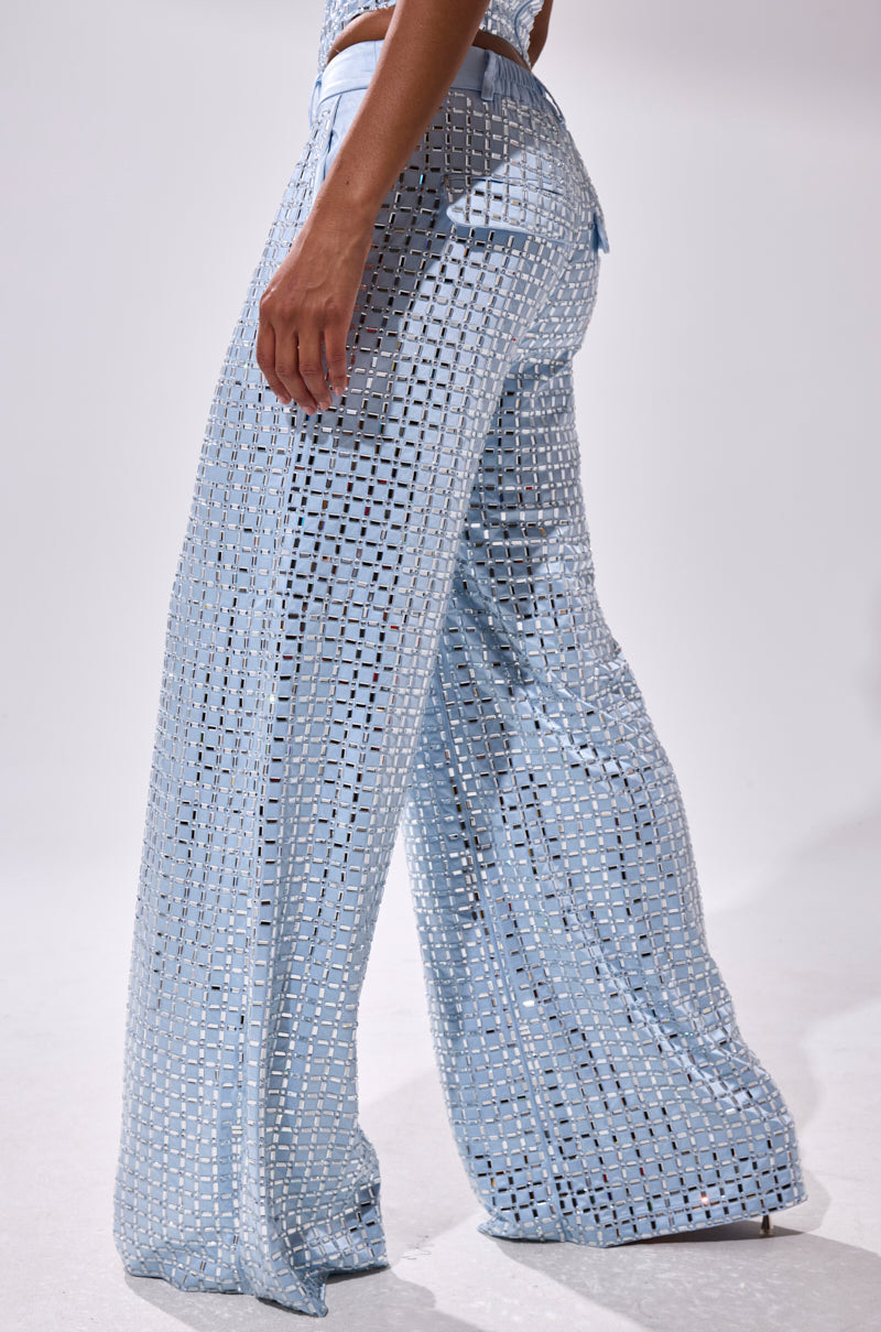 A person stands sideways against a plain white background wearing LILA EMBELLISHED SATIN TROUSER in powder blue with a square cutout pattern and wide leg design.