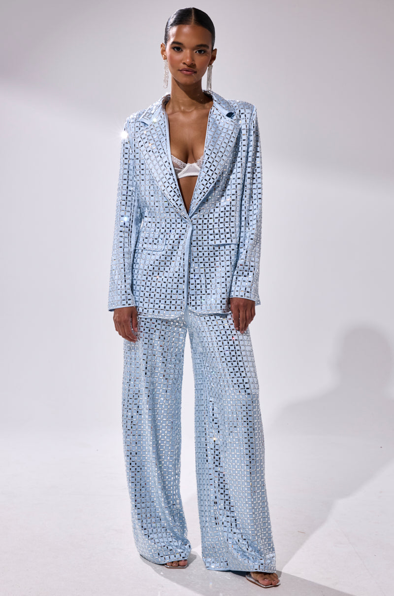 A woman poses confidently against a plain light background, wearing the LILA EMBELLISHED SATIN TROUSER in powder blue with a matching sequin blazer over a white bralette and her hair pulled back.