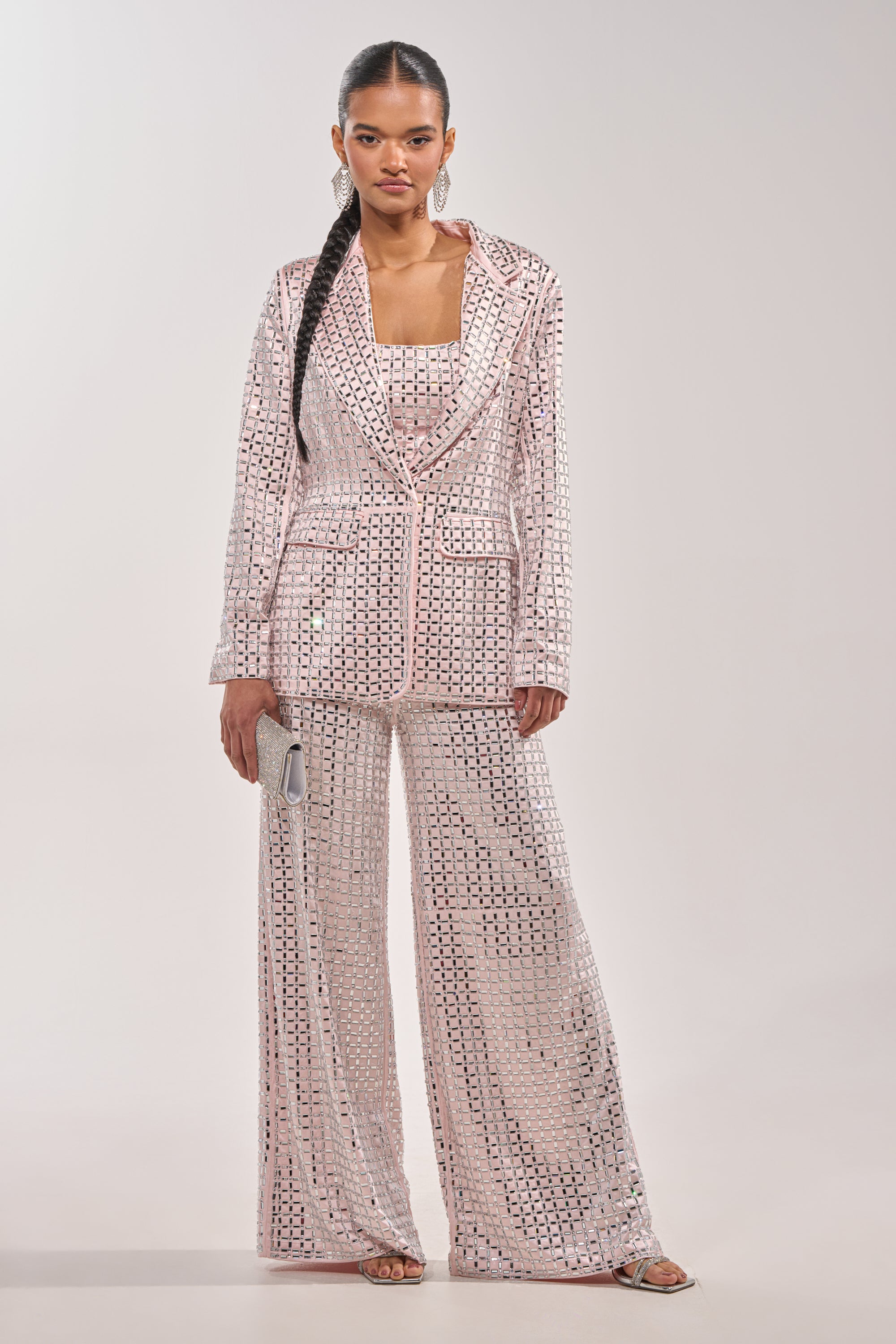 A woman wears the LILA EMBELLISHED SATIN BLAZER IN LIGHT PINK, covered in sparkling square sequins. She pairs it with a matching top, a silver clutch, open-toed heels, and styles her long hair in a sleek braid. 7