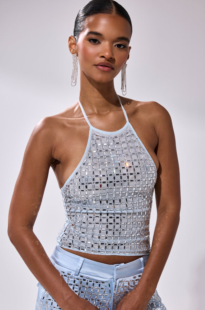 A woman with slicked-back hair wears the LILA EMBELLISHED MOCK NECK MESH TOP and silver sequin pants. She has long dangling earrings and stands against a plain light background, looking confidently at the camera.