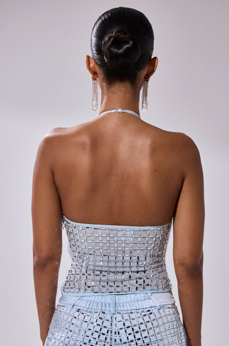 A woman with her hair in a sleek bun models the LILA EMBELLISHED MOCK NECK MESH TOP and matching pants. She faces away, revealing her bare back and statement earrings against a light, plain background.