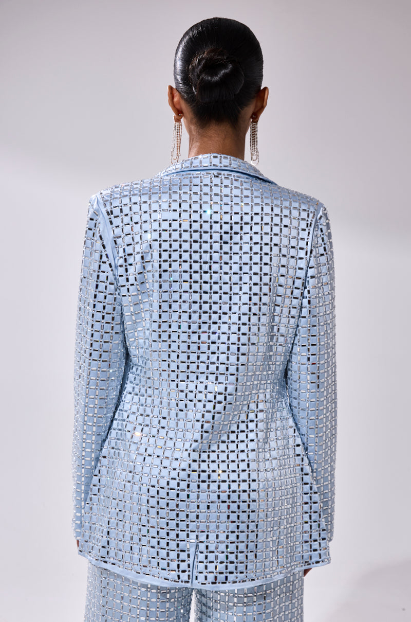 A person with dark hair in a sleek bun is seen from behind, wearing the LILA EMBELLISHED SATIN BLAZER and matching pants with a square geometric cut-out pattern, paired with long, dangling earrings.