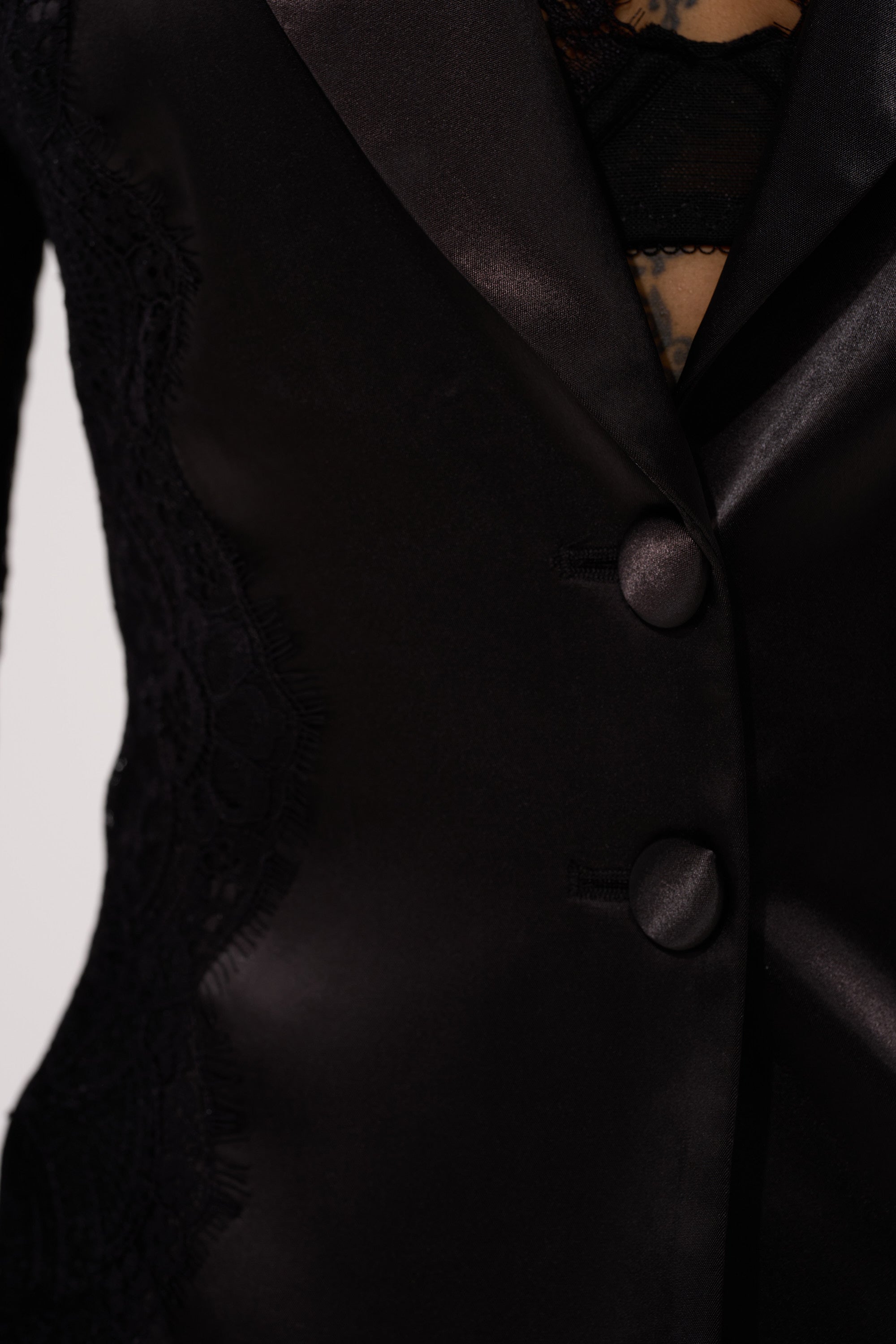 Close-up of the AU CONTRAIRE LACE SATIN BLAZER—a black satin blazer with two buttons and lace side detailing—styled over a dark lace top. 9