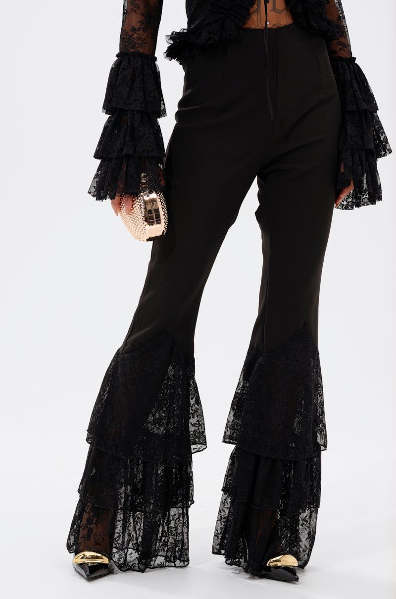A person wears LOOKS AND FEELS GOOD LACE FLARE LEGGING with tiered lace ruffles at the calves, matching ruffle sleeves, a gold clutch, and black pointed heels with gold tips, all set against a plain white background. 2