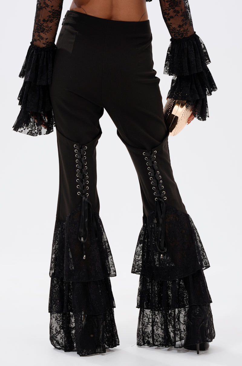 A person wears LOOKS AND FEELS GOOD LACE FLARE LEGGING—high-rise black lace pants with lace-up back details and tiered ruffle hems—paired with a matching lace sleeve top. The photo is taken from behind. 4