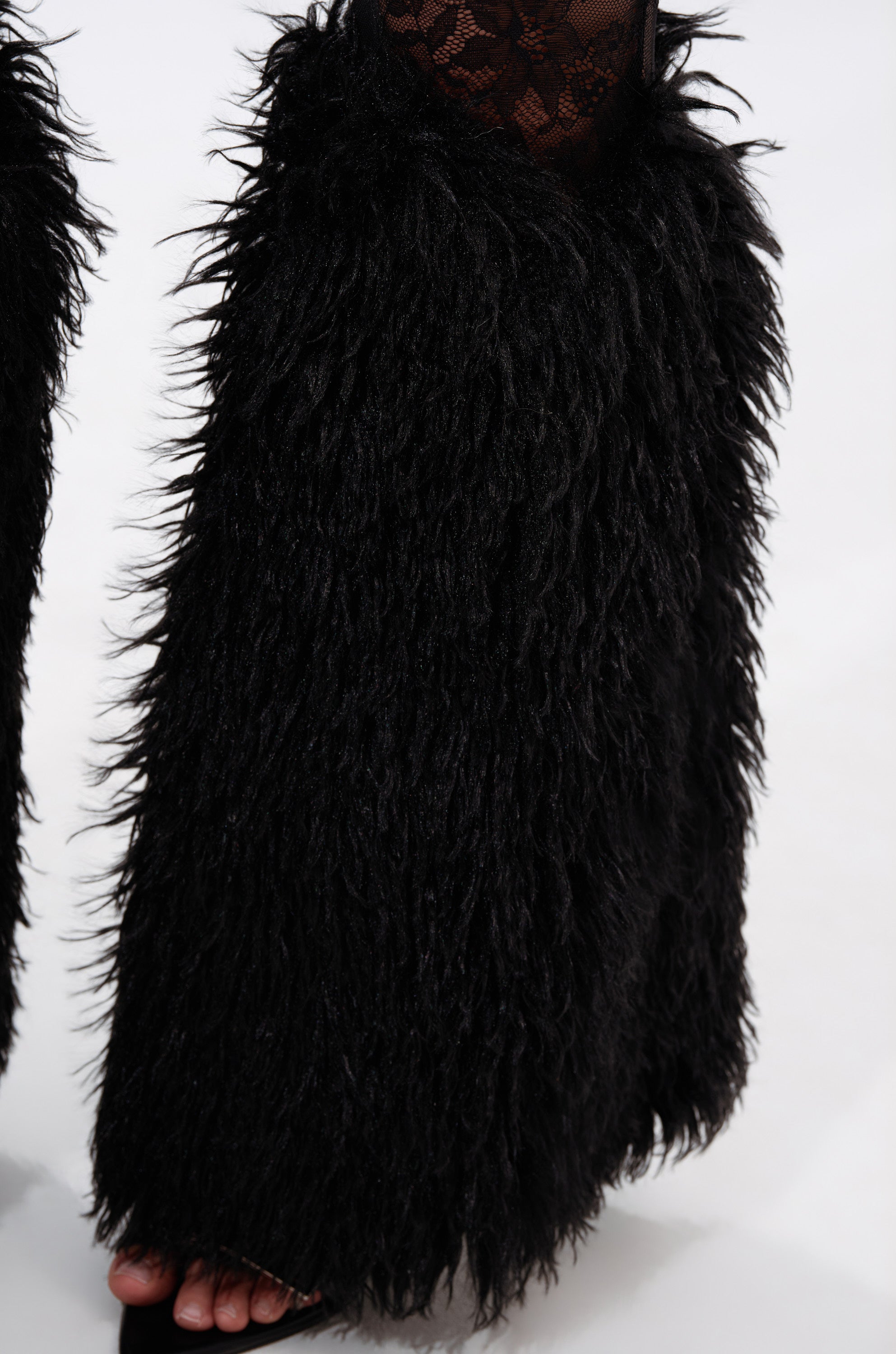 A close-up shows someone wearing the FEELING GOOD LACE LEGGING WITH FUR TRIM, featuring black shaggy faux fur over lace leggings, with toes visible in open-toe shoes against a light background. 7