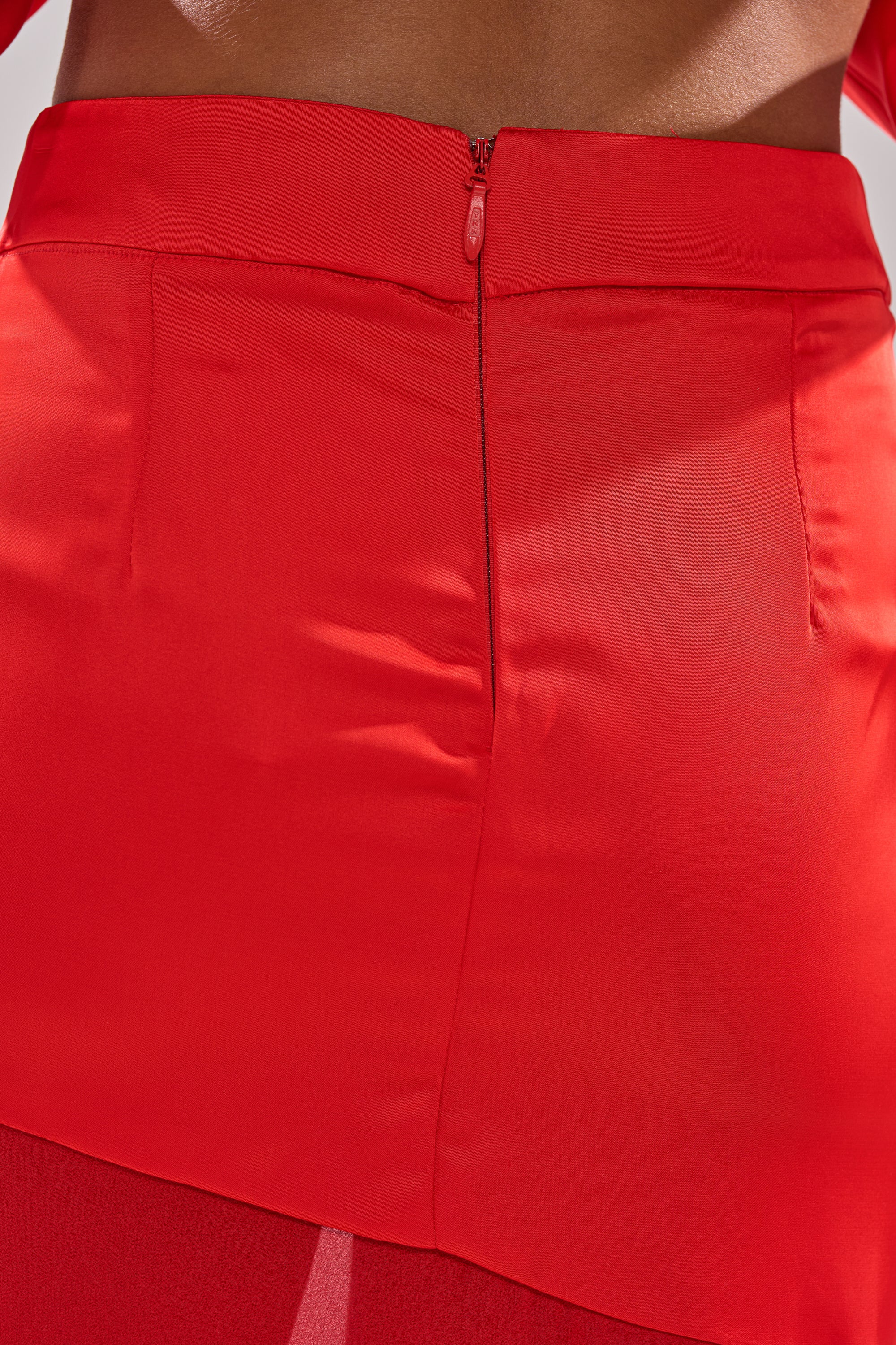 Close-up of the back of the RED HOT ASYMMETRICAL MIDI SKIRT in bright red, featuring a high waist, visible zipper, and waist seam. The smooth, slightly shiny fabric gives it a satin-like midi skirt appearance. 6