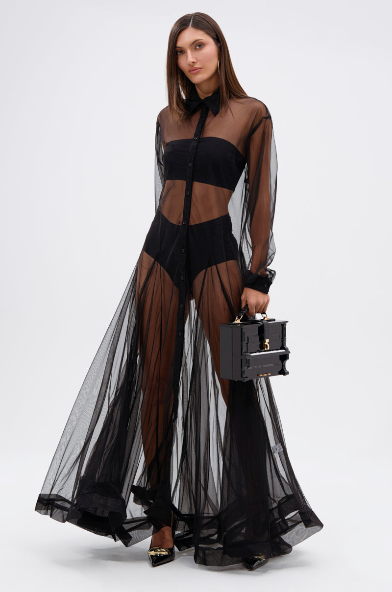 A woman models the COOL GIRL MESH LAYERING MAXI DRESS—a sheer mesh, button-down, collared maxi with long sleeves—over black underwear and heels. She holds a small black box handbag and stands against a white background.